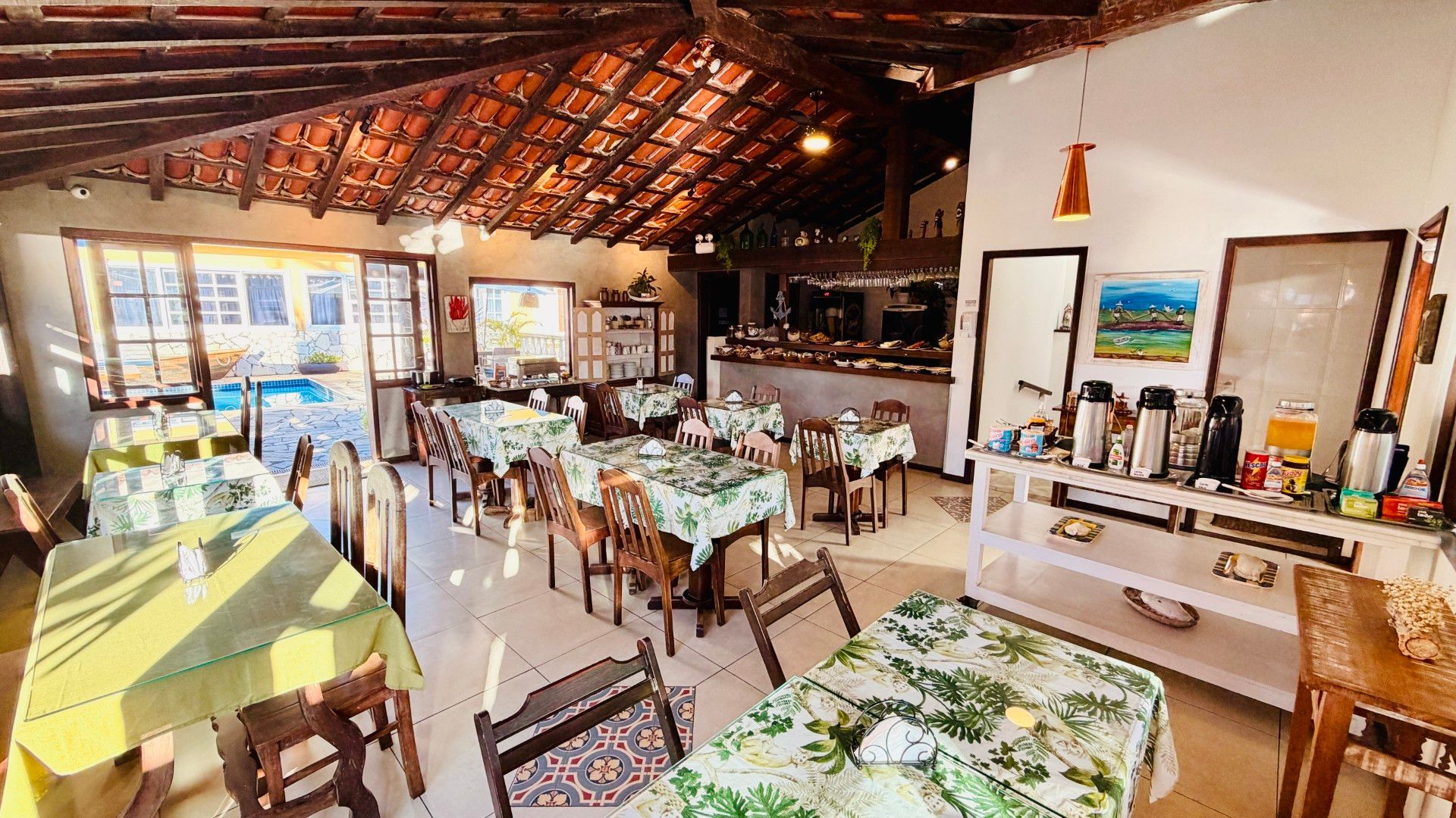 Balcão de buffet com bandejas de comida, pratos e uma mulher em pé em uma área de refeições estilo cafeteria.