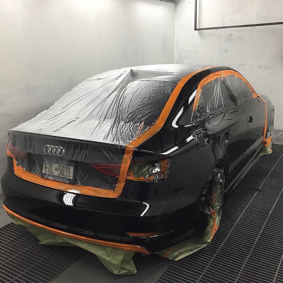 A black car is being painted in a paint booth.