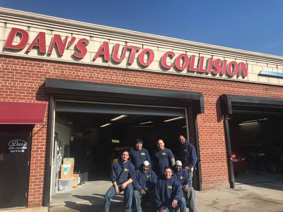 A group of men are posing for a picture in front of dan 's auto collision.