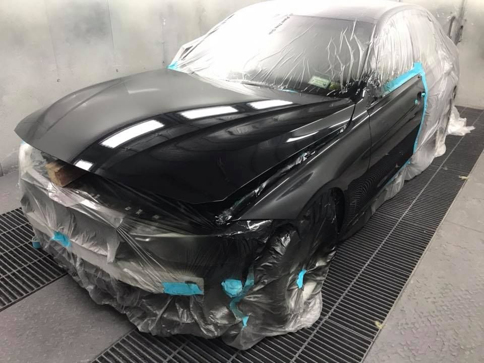 A black car is wrapped in plastic and sitting in a paint booth.