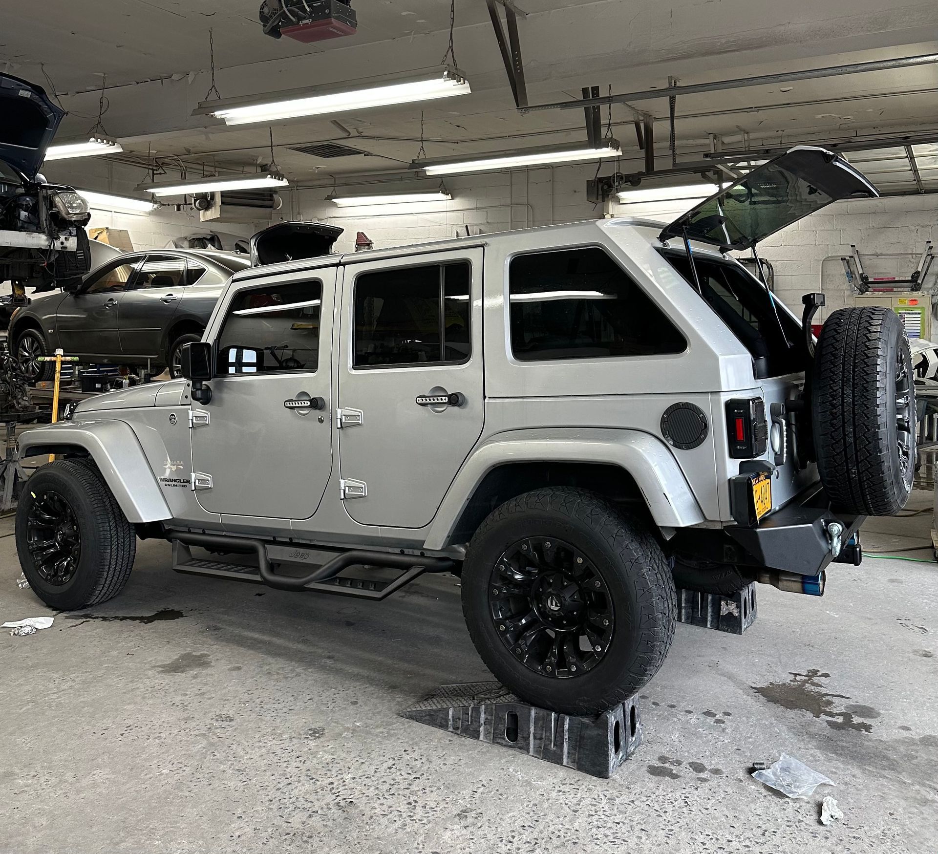 A silver jeep is parked in a garage with its trunk open.