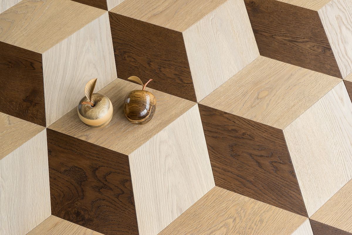 Two wooden apple sculptures on a floor with a 3D cube pattern in light and dark brown.