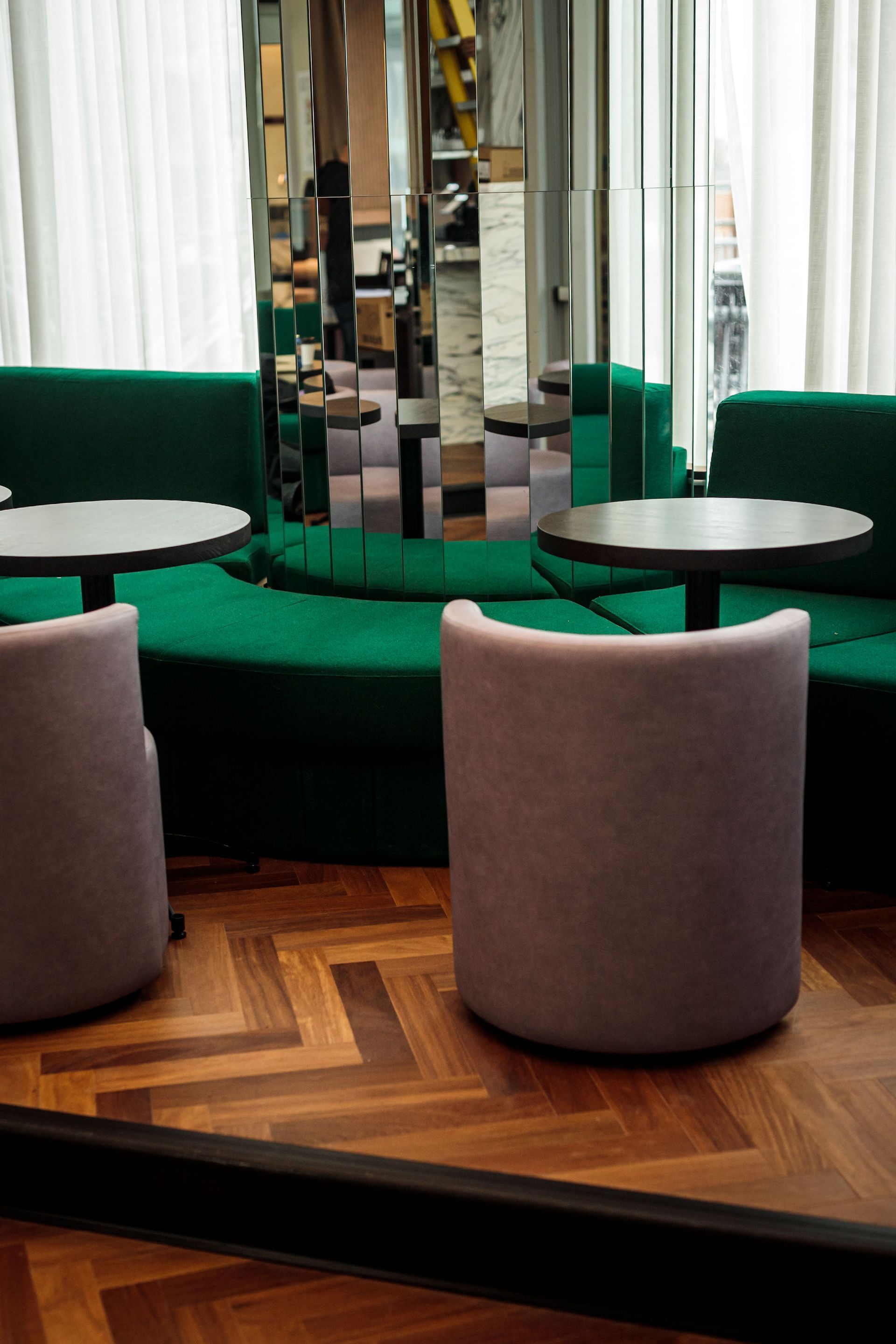 Salon élégant avec sièges verts, tables rondes et mur de miroirs sur parquet