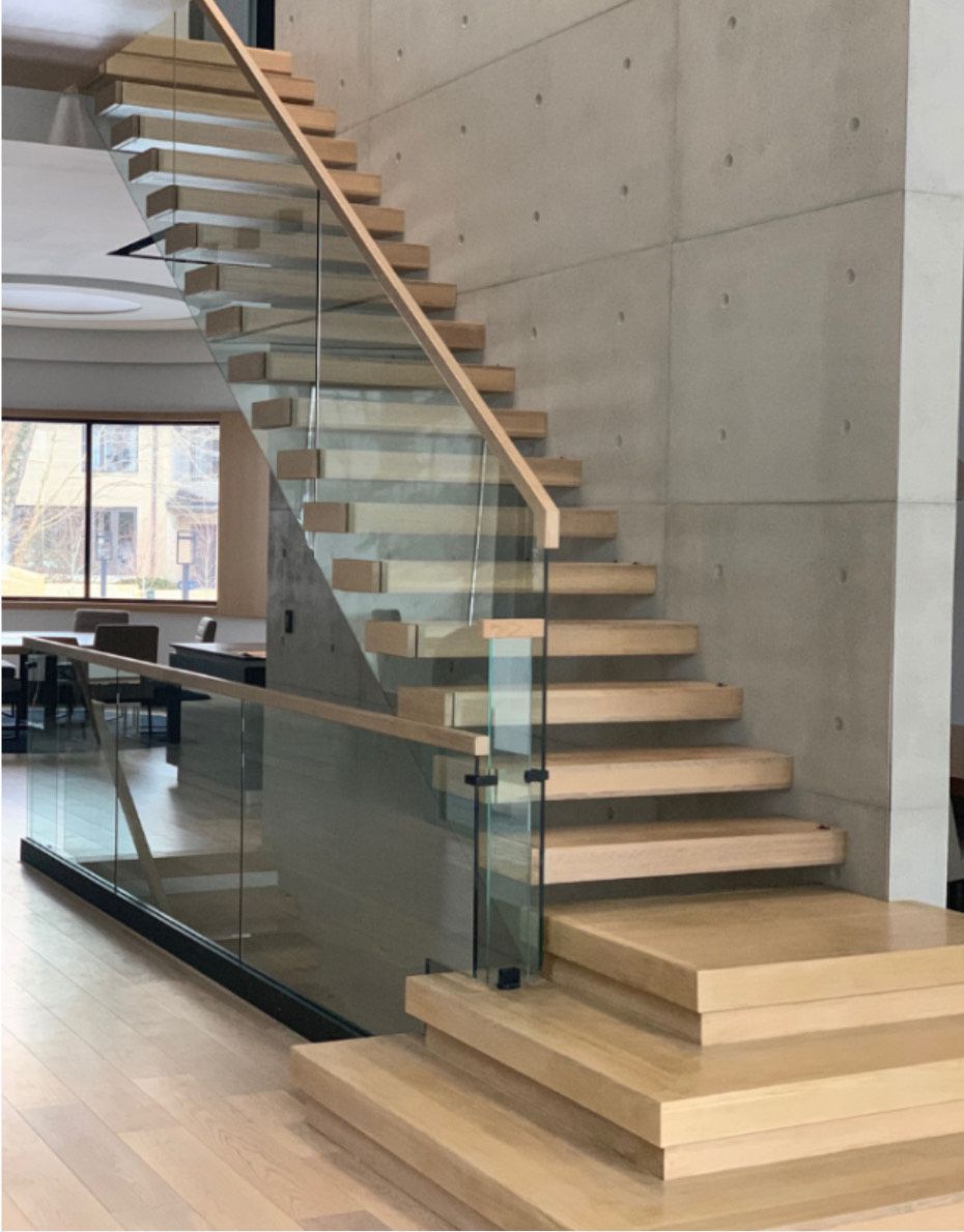 Modern wooden staircase with glass railing and concrete wall.