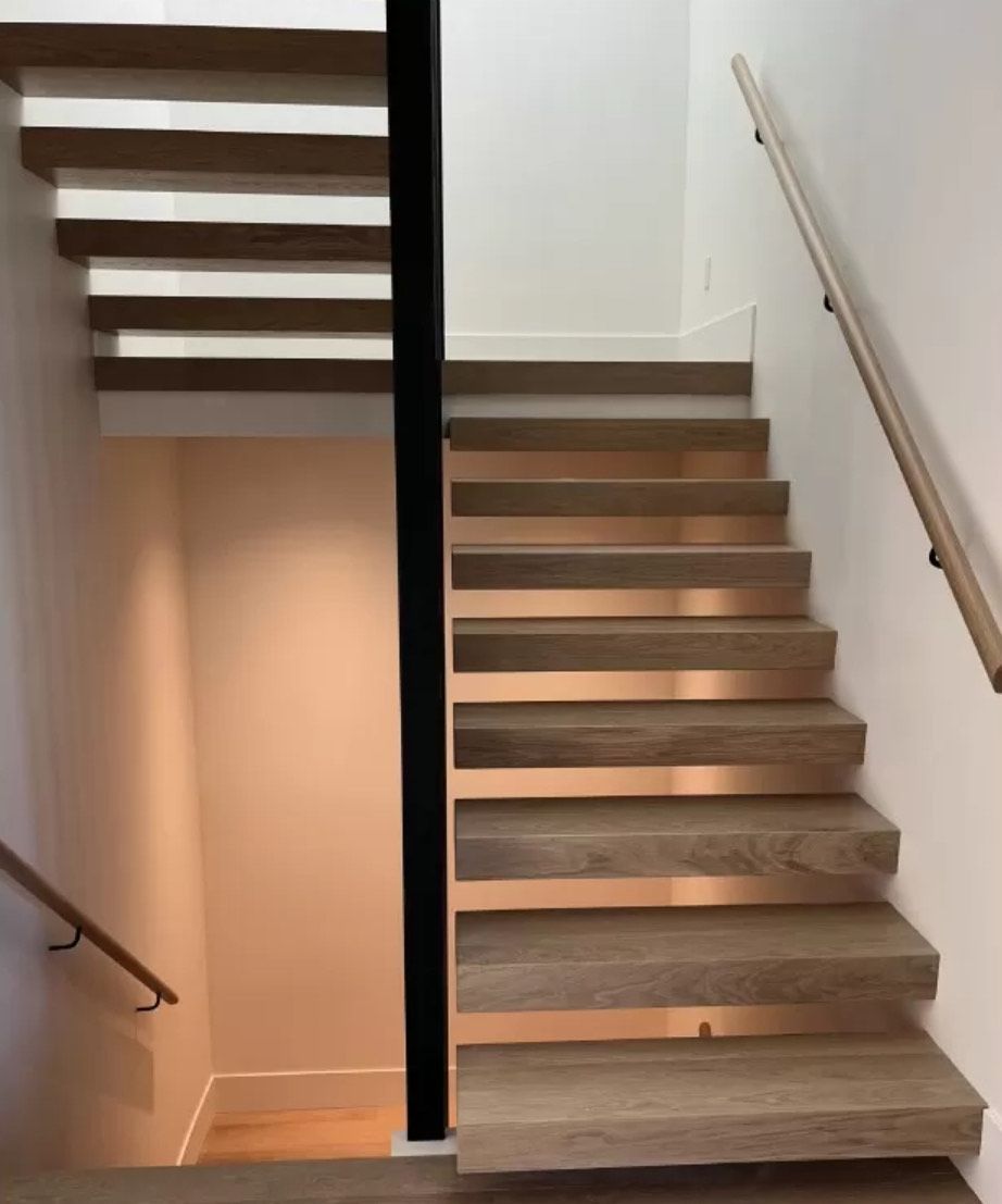 Modern wooden staircase with copper accents and black support beam, white walls, wood handrails.