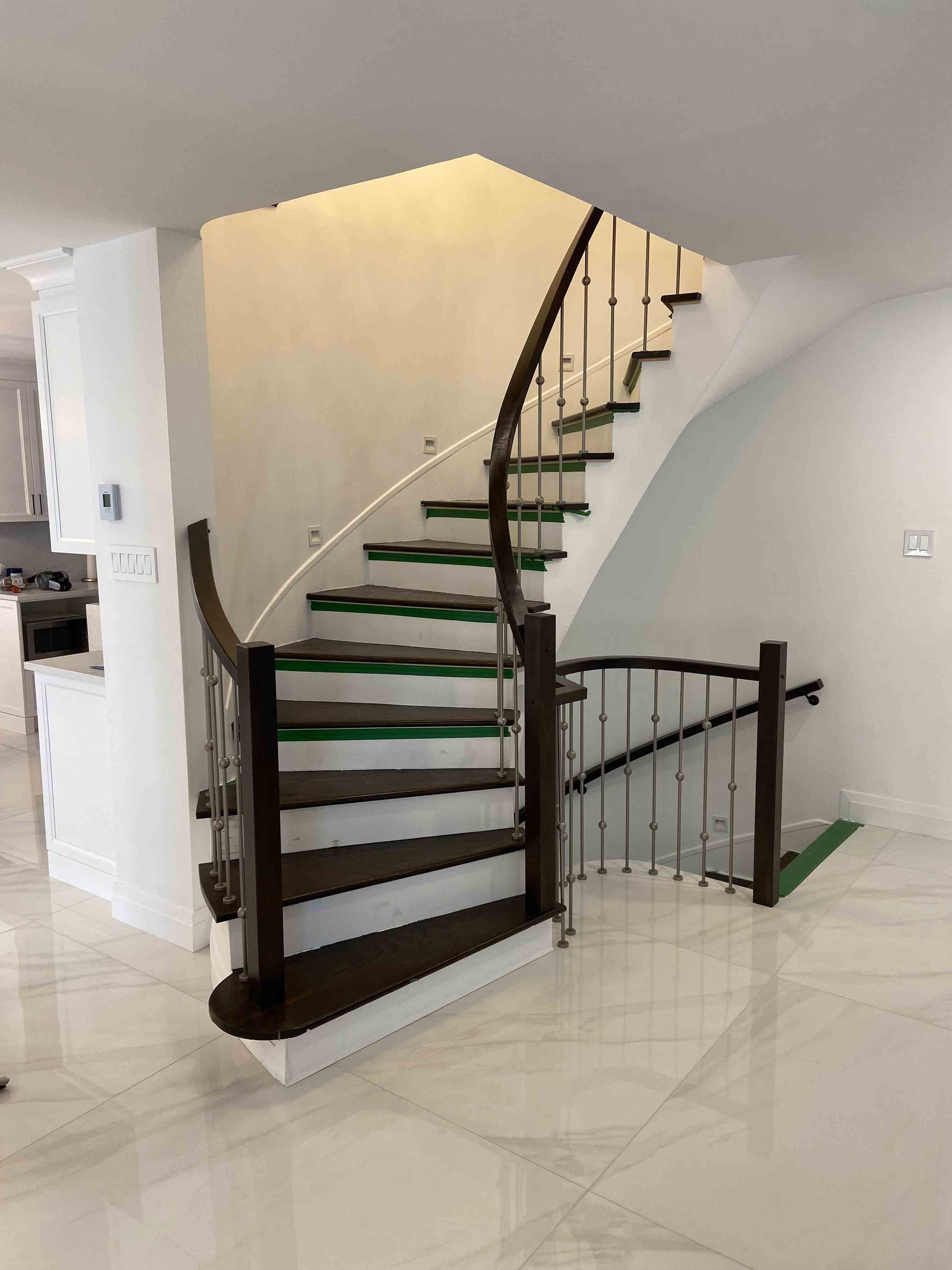 Escalier courbe avec rampe foncée et marches en bois dans un intérieur de maison moderne et lumineux