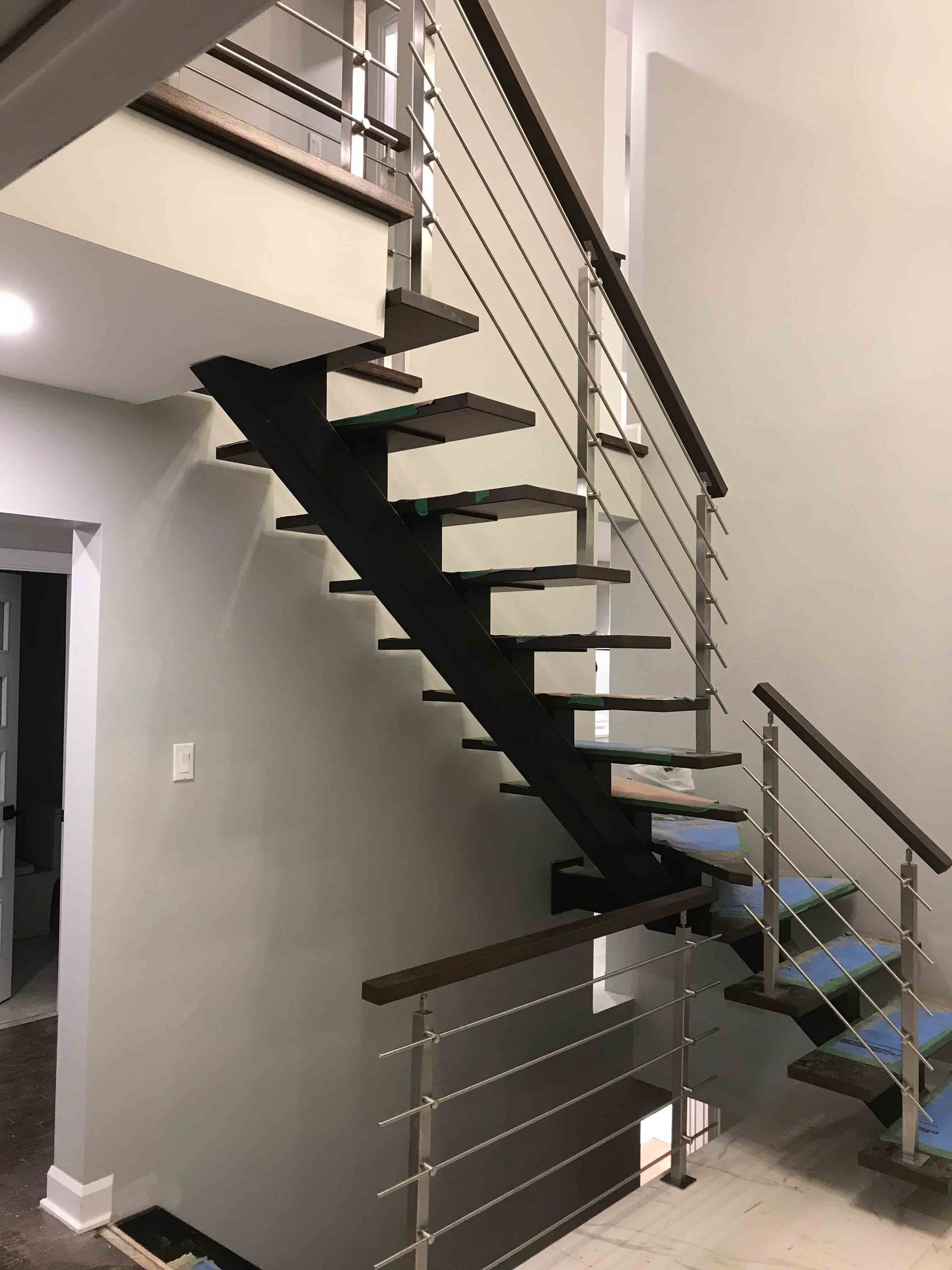 Escalier intérieur moderne avec marches noires, rampes en métal et murs blancs dans un intérieur lumineux