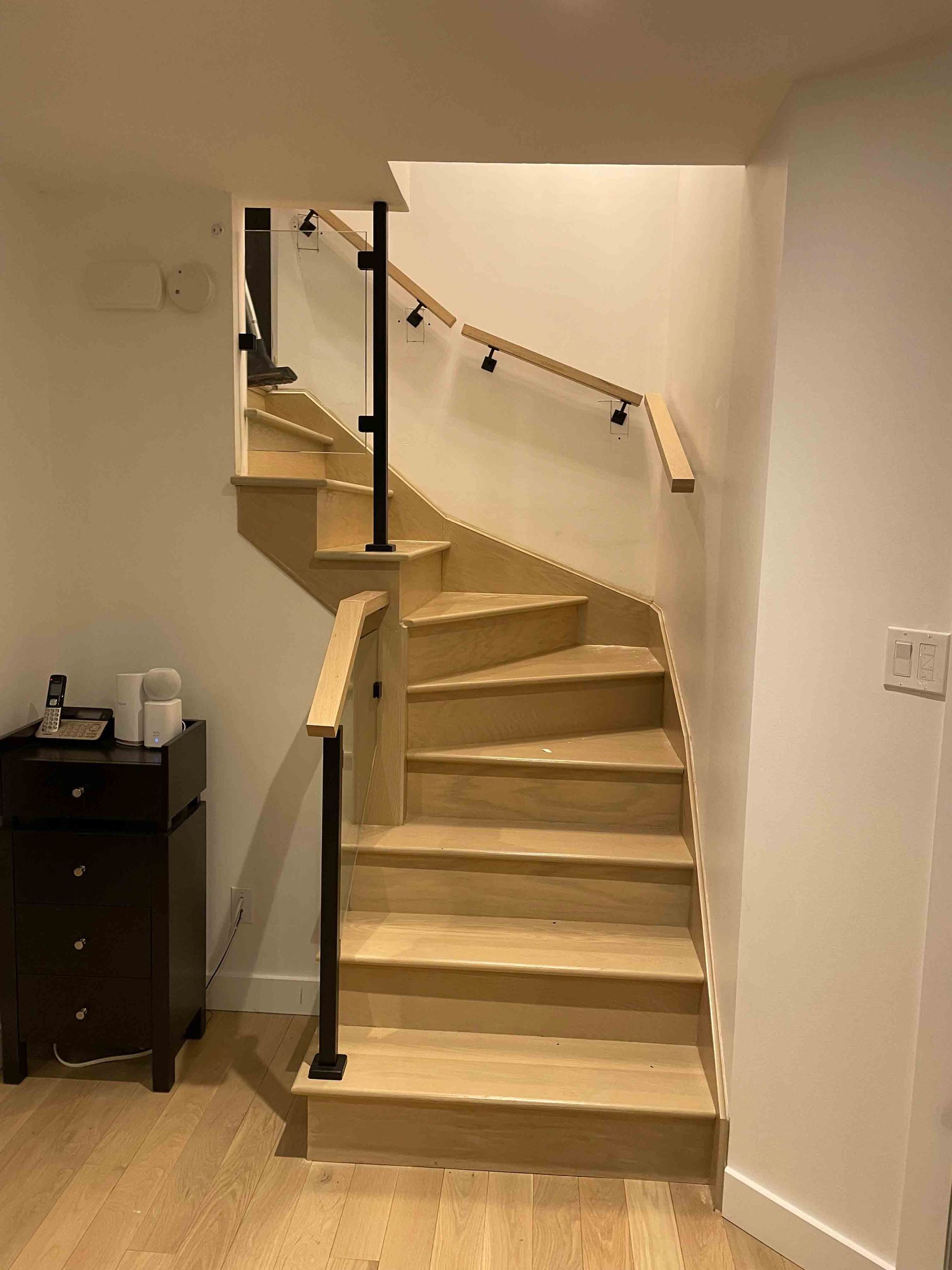 Escalier beige incurvé avec rampe noire dans un couloir intérieur blanc