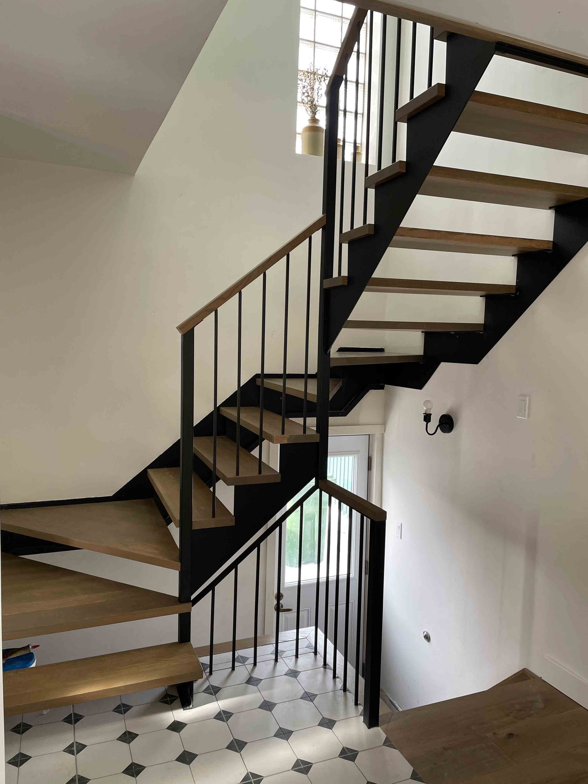 Escalier intérieur en colimaçon moderne avec rampe noire et marches en bois dans une entrée aux murs blancs