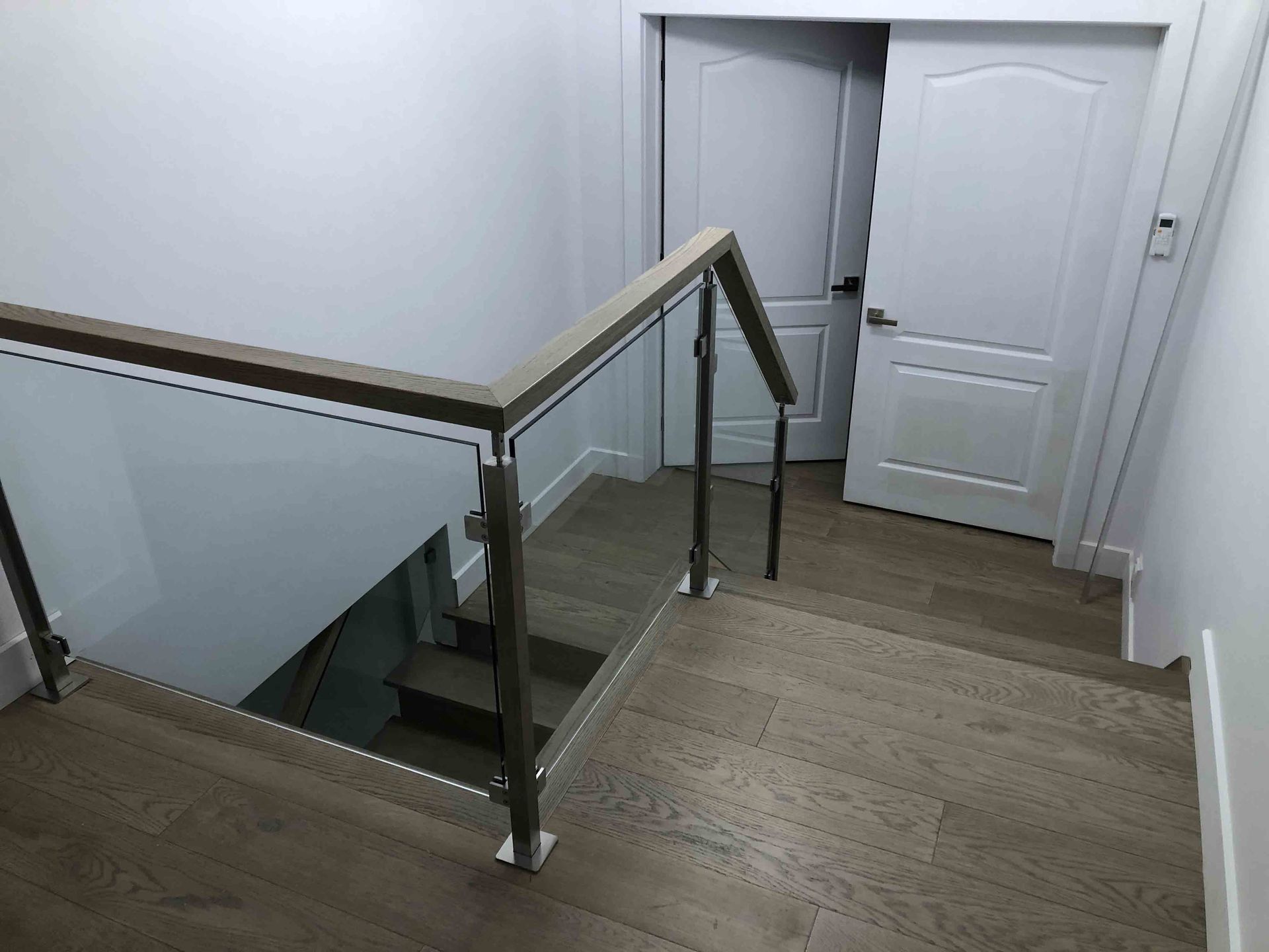 Un intérieur moderne avec un escalier en bois gris. Une étagère intégrée avec des livres se trouve près de l'escalier. Les murs sont blancs.