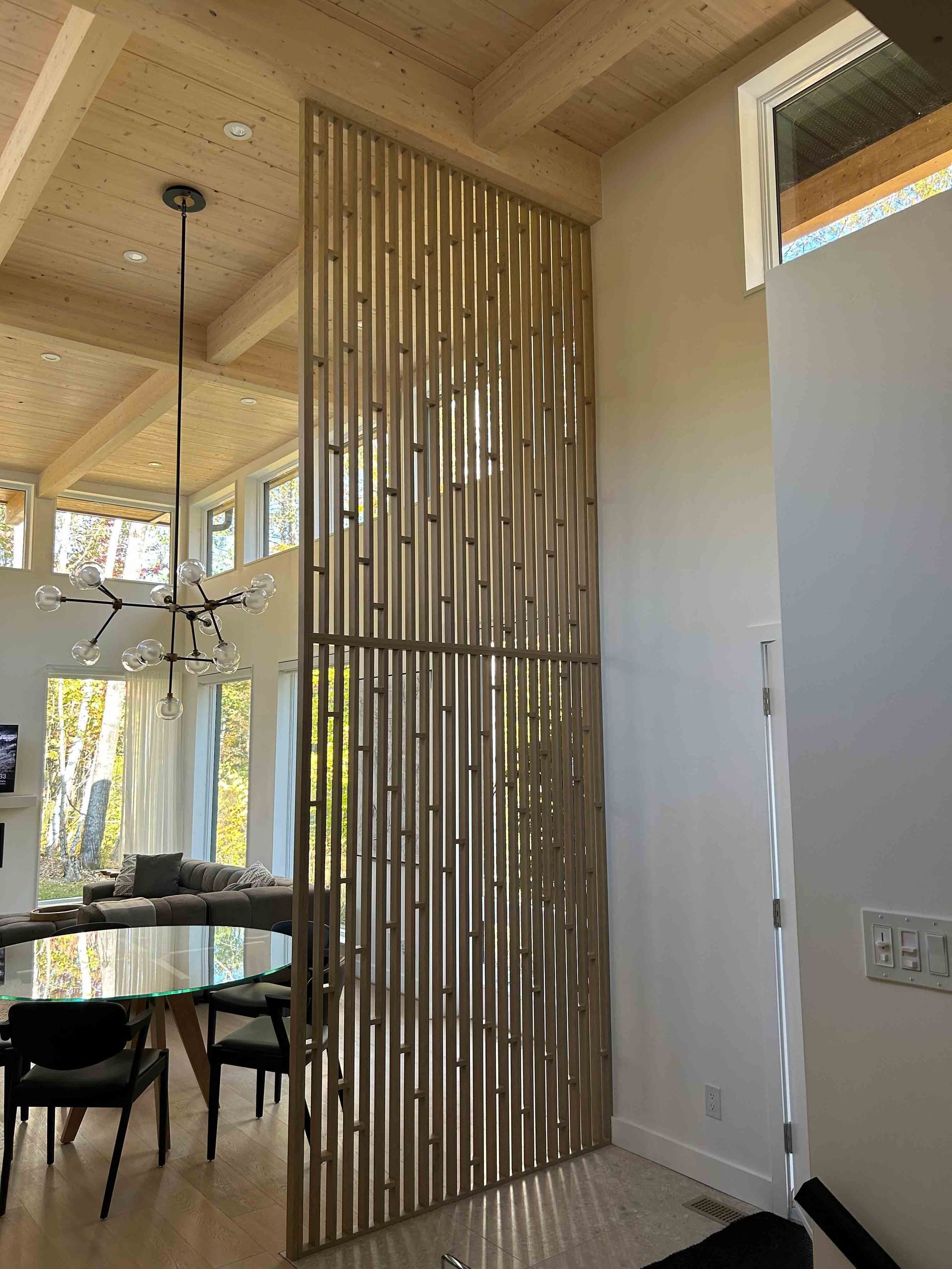 Coin repas avec cloison en bambou, table ronde, chaises et haut plafond avec suspension lumineuse.