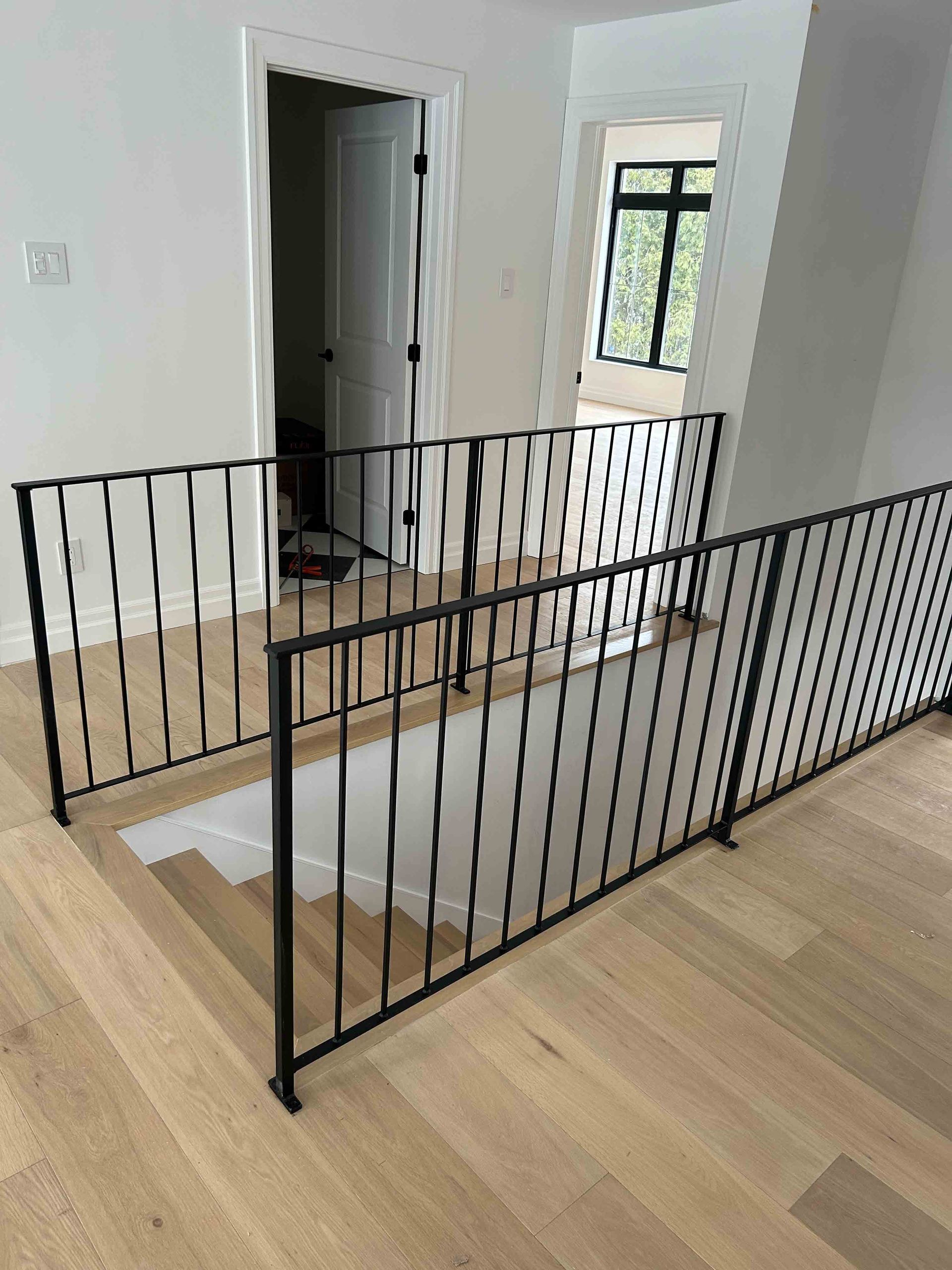 Rambarde d'escalier en métal noir autour d'une cage d'escalier dans une pièce lumineuse avec parquet clair et murs blancs