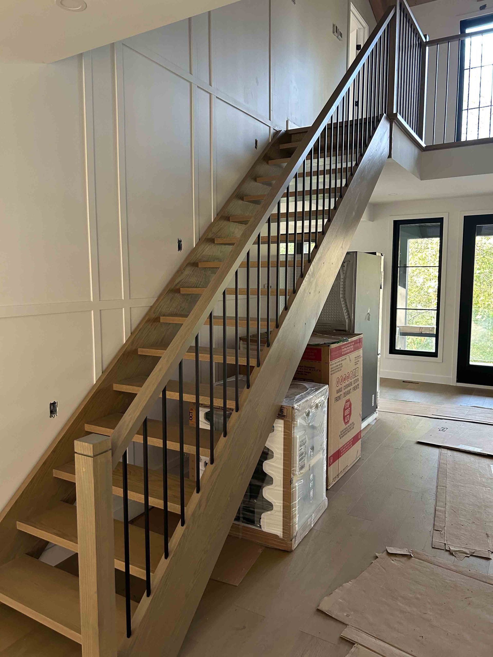 Escalier intérieur en construction avec marches en bois non finies, rampes noires et matériaux entreposés en dessous.