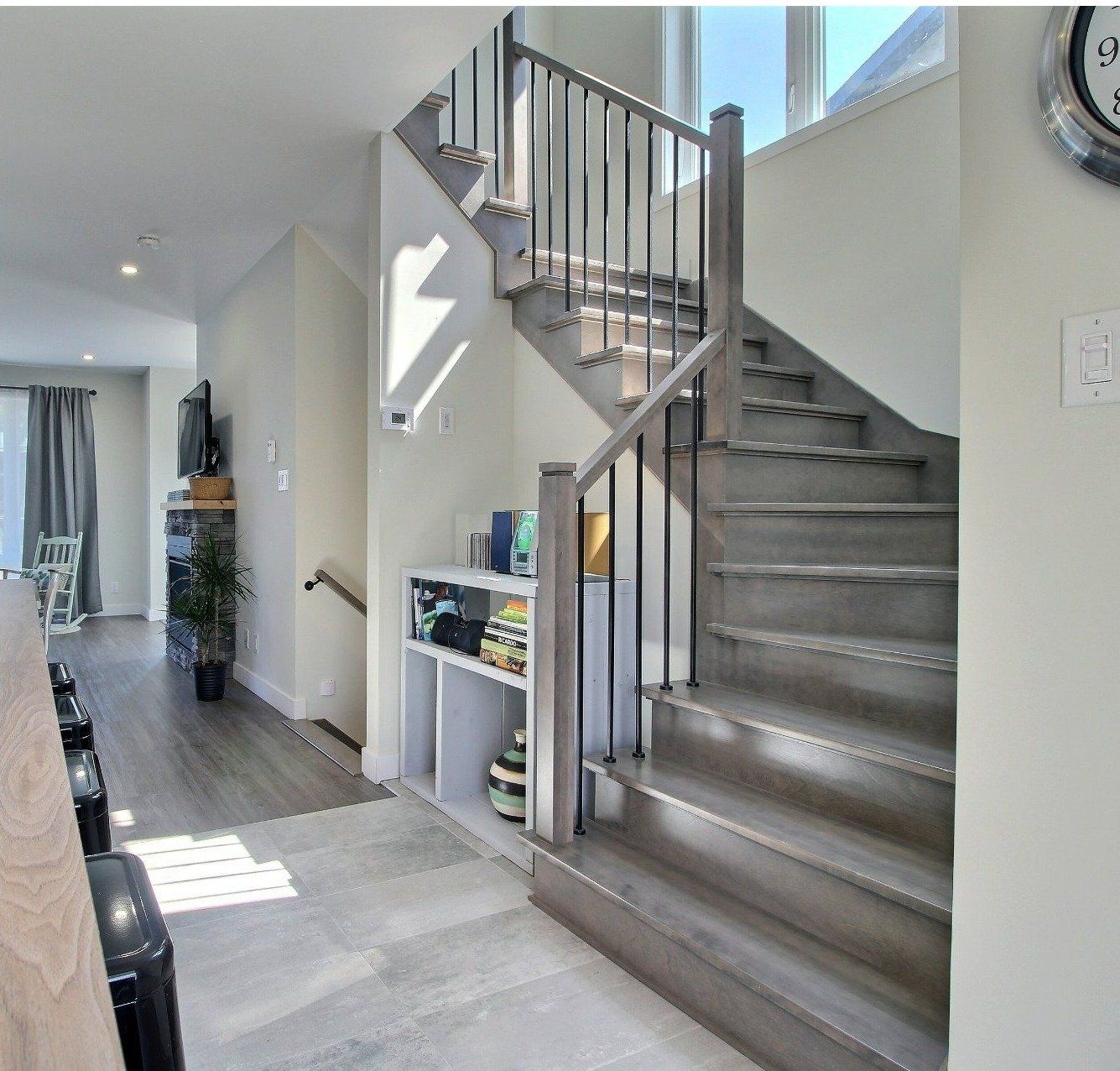 Un intérieur moderne avec un escalier en bois, des murs gris clair et une petite étagère intégrée. La pièce paraît lumineuse et aérée.
