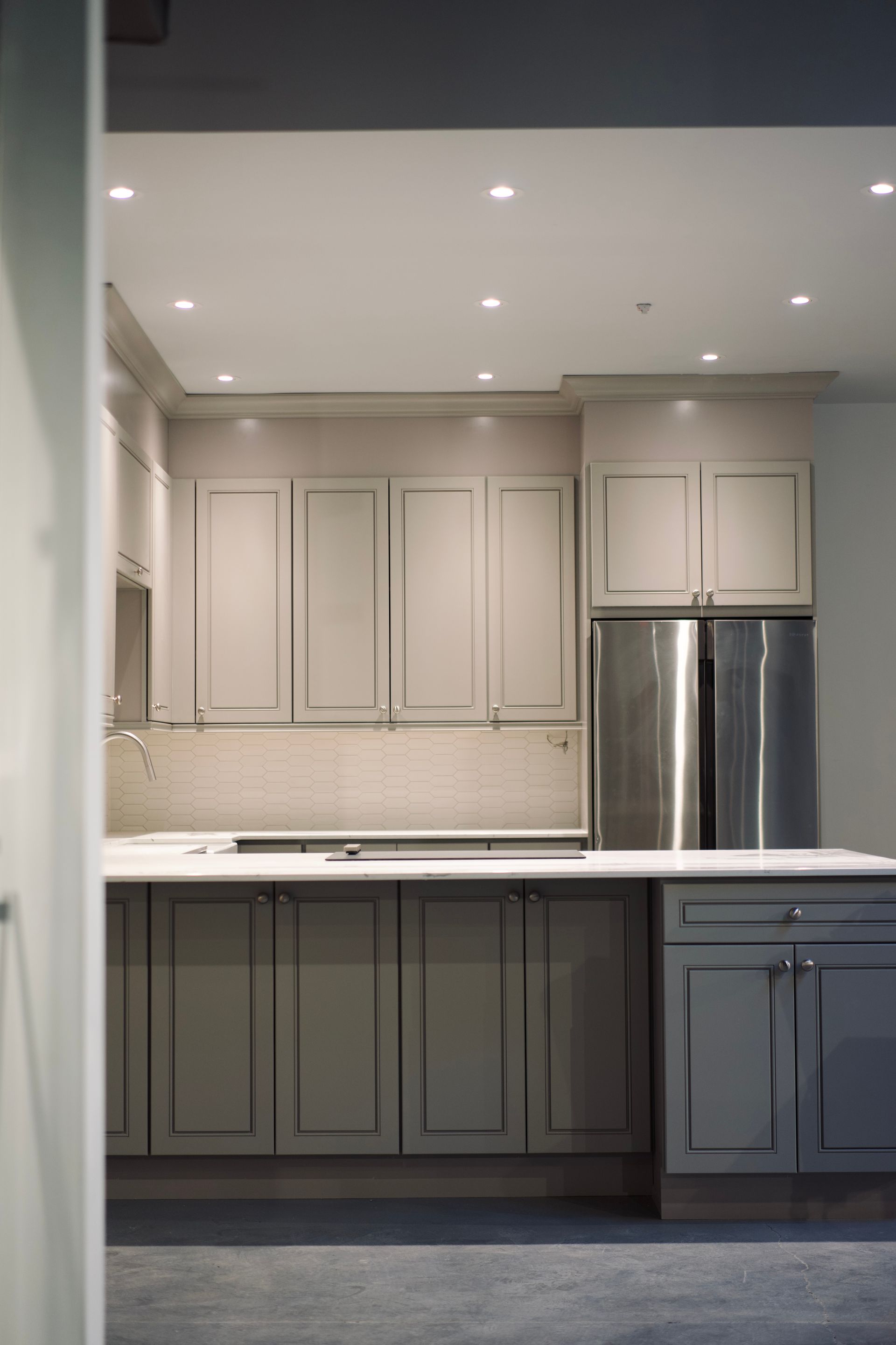 A kitchen with gray cabinets and a stainless steel refrigerator
