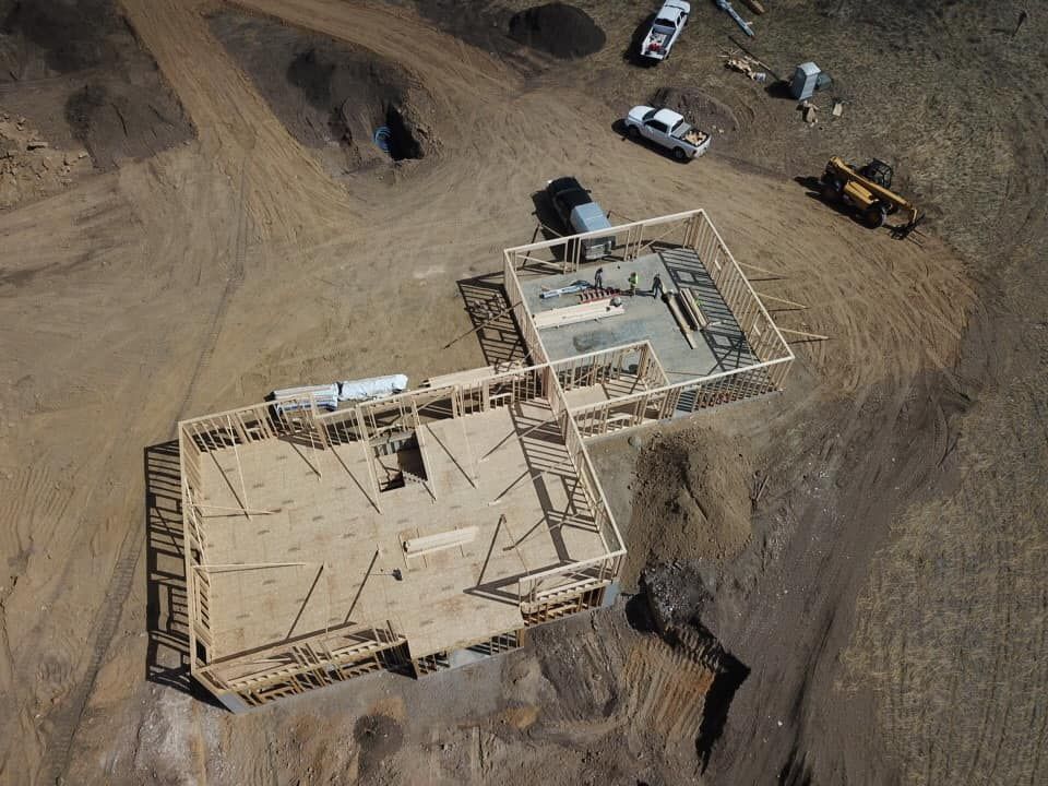 Aerial view of a house under construction; wooden frames with concrete foundations on a dirt lot, with construction vehicles.