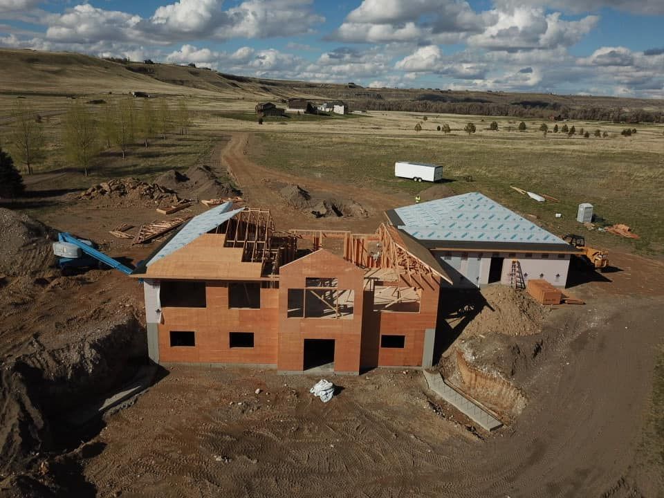 House under construction with exposed framing in a rural landscape.