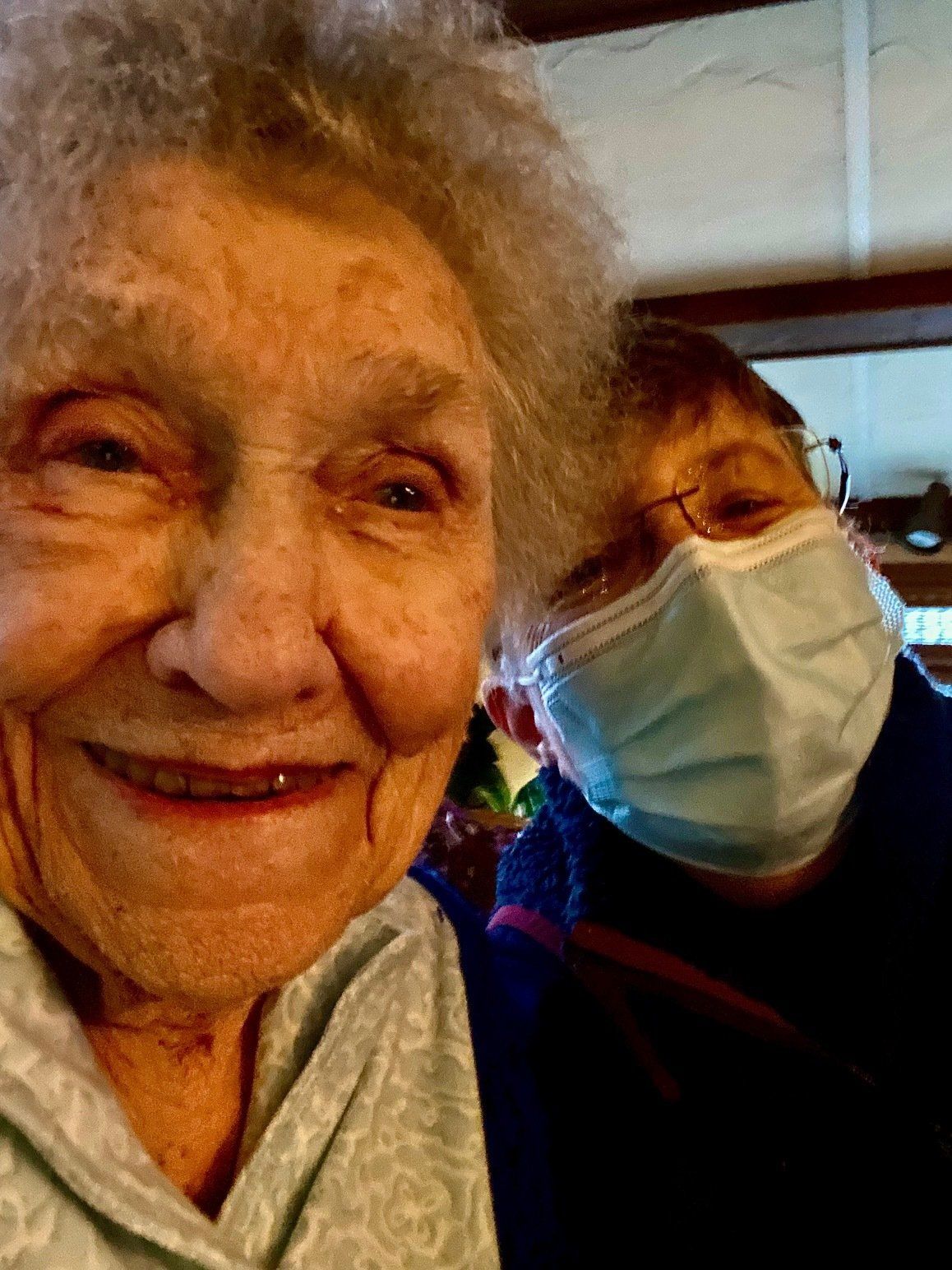 Two elderly women wearing face masks are taking a selfie together.