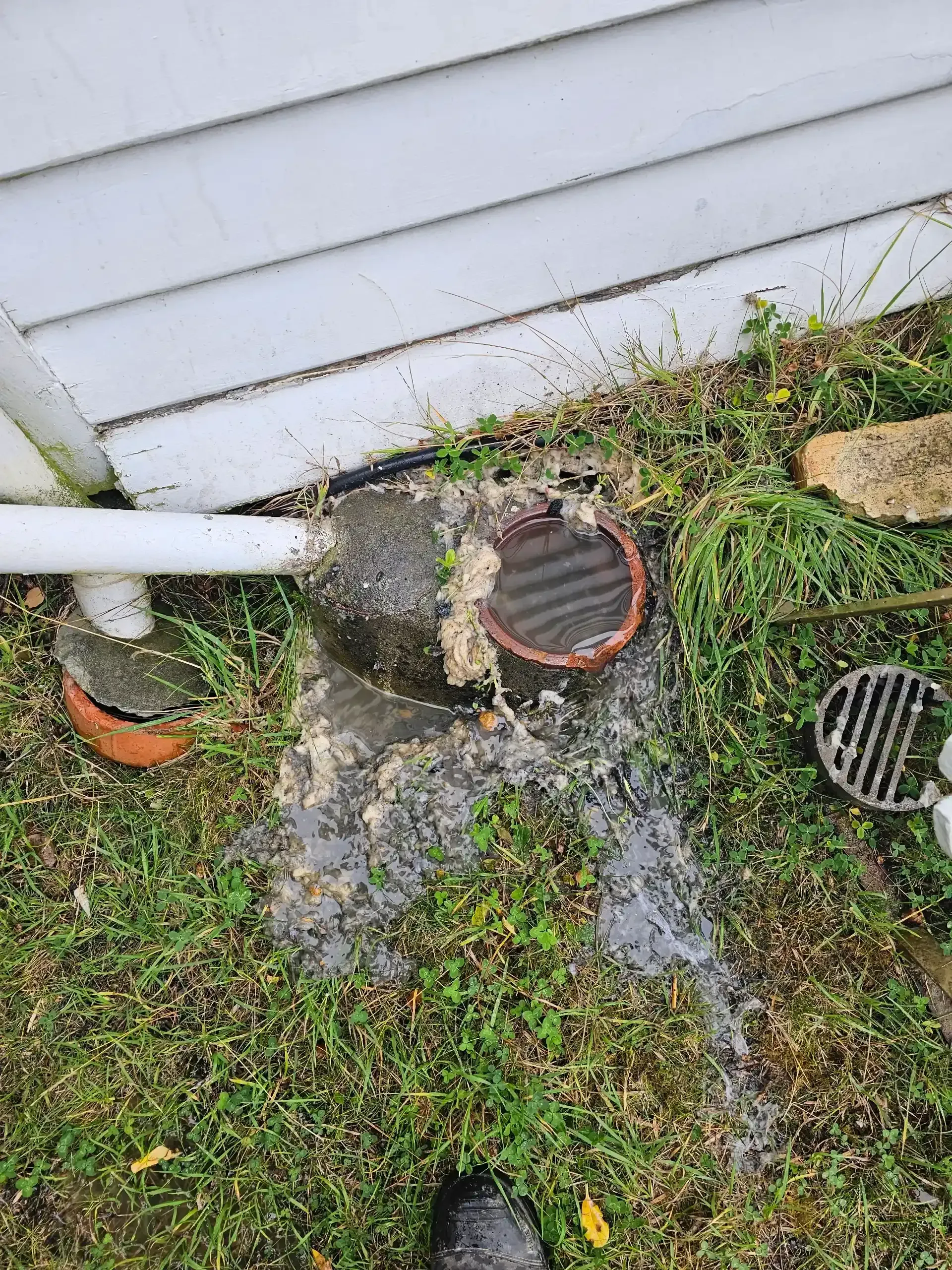 A clogged, overflowing drainage pit next to a white house wall with a white pipe leading into it. — Lenny's Plumbing & Contracting in Granton, TAS