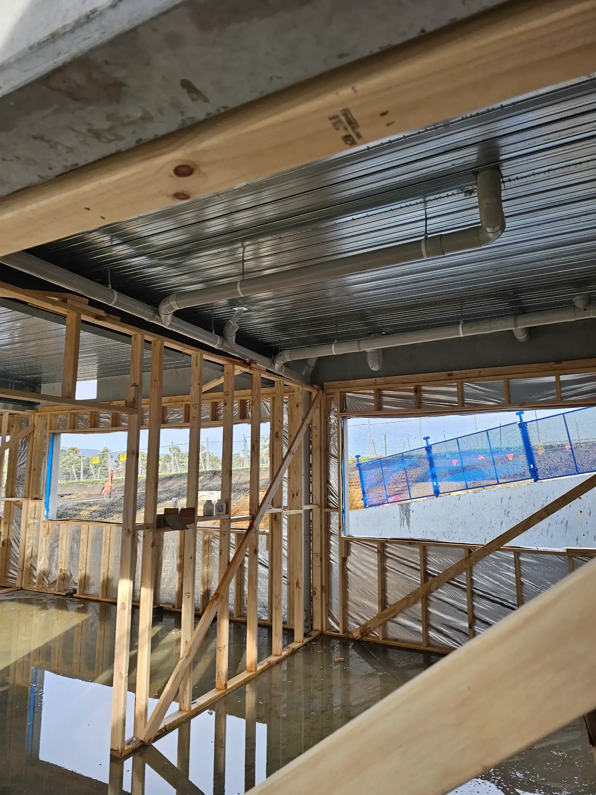 Interior construction of a room with exposed wooden wall framing, metallic ceiling insulation, and white plastic plumbing. — Lenny's Plumbing & Contracting in Granton, TAS
