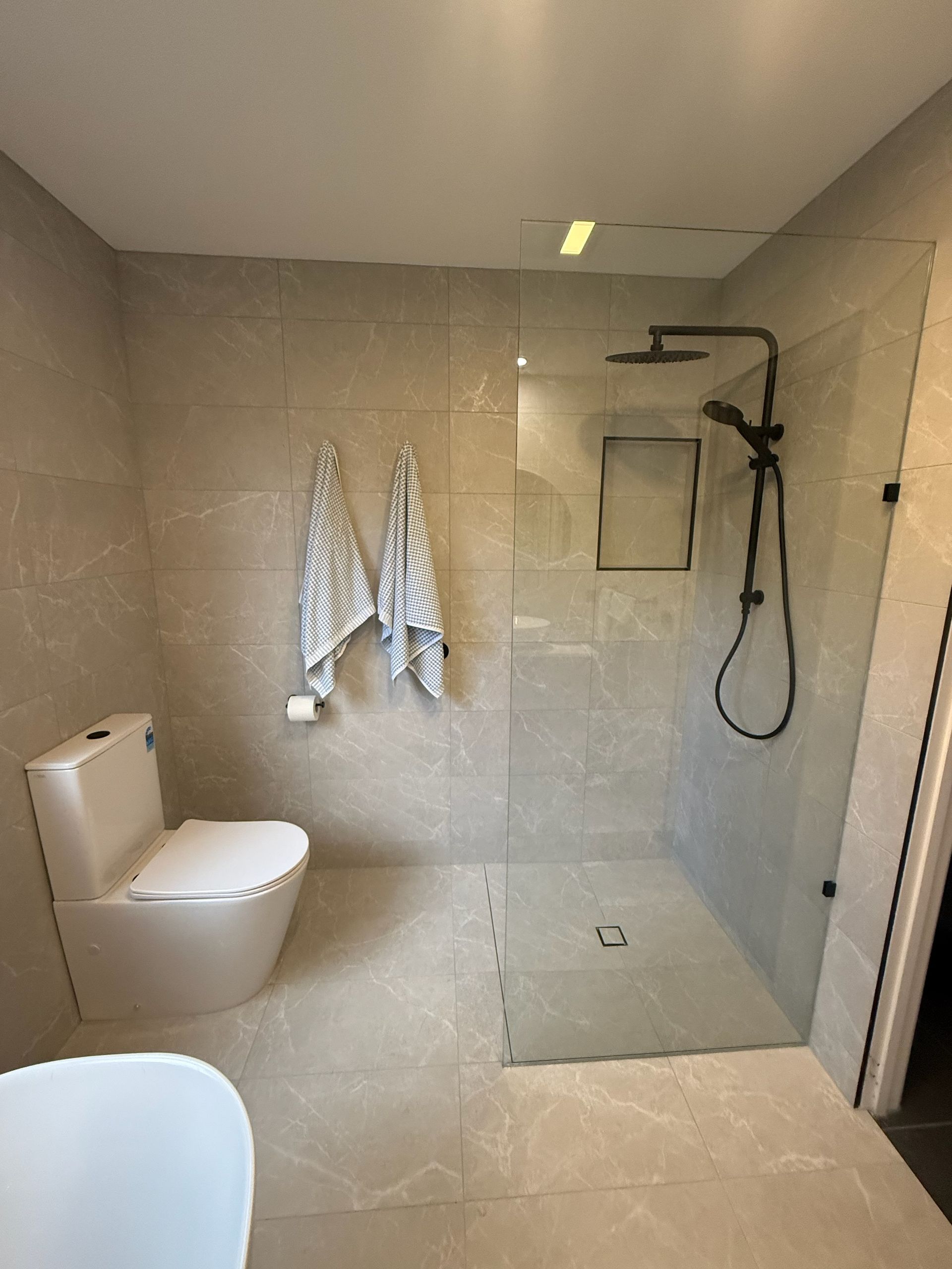 A modern beige bathroom with a toilet and a walk-in glass shower — Lenny's Plumbing & Contracting in Granton, TAS