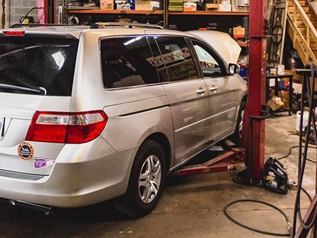 A silver minivan is sitting on a lift in a garage.