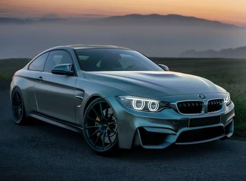 Silver BMW M4 coupe on a road, with a mountain range in the background.