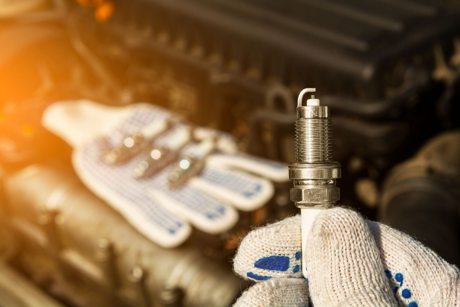 A person is holding a spark plug in their hand in front of a car engine.