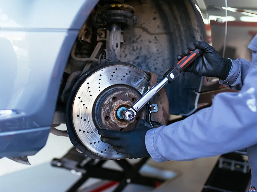 A man is working on the brake disc of a car with a wrench.