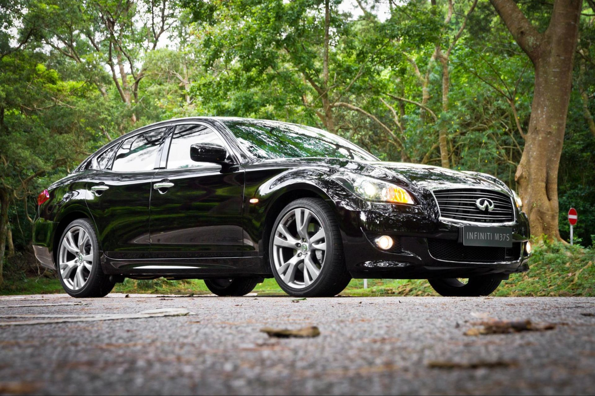 a black car is parked on the side of a road in front of trees .