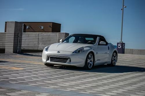 White Nissan 370Z convertible parked on a parking garage deck, under a blue sky.