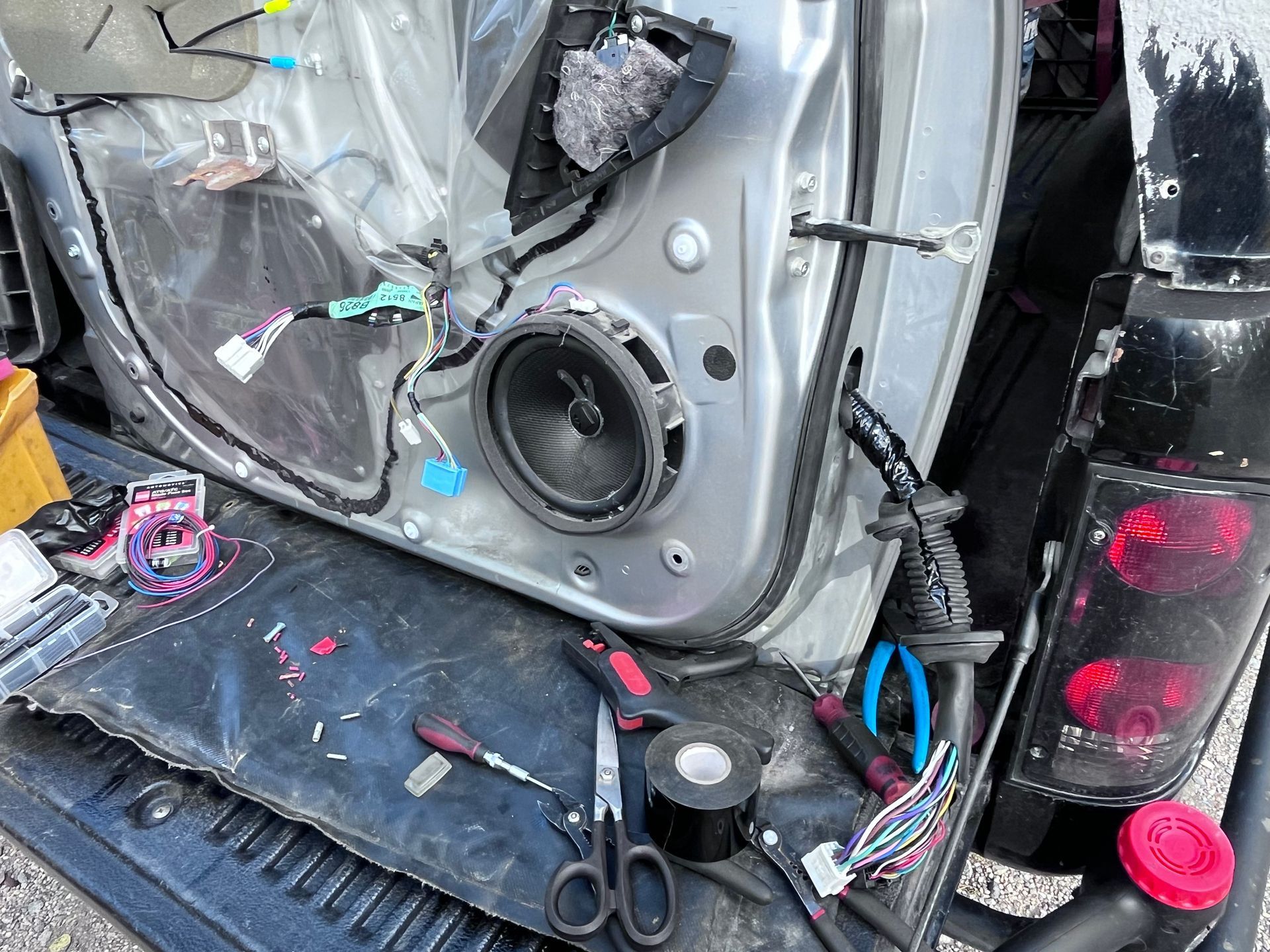 Damaged car door interior with exposed wiring, speakers, and tools in the cargo area