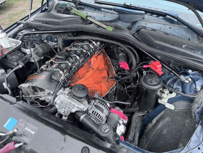 Car engine bay with a bright orange engine cover and red battery terminals under the hood
