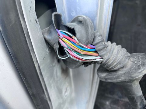 Multicolored wires exposed through a damaged rubber grommet in a vehicle door frame