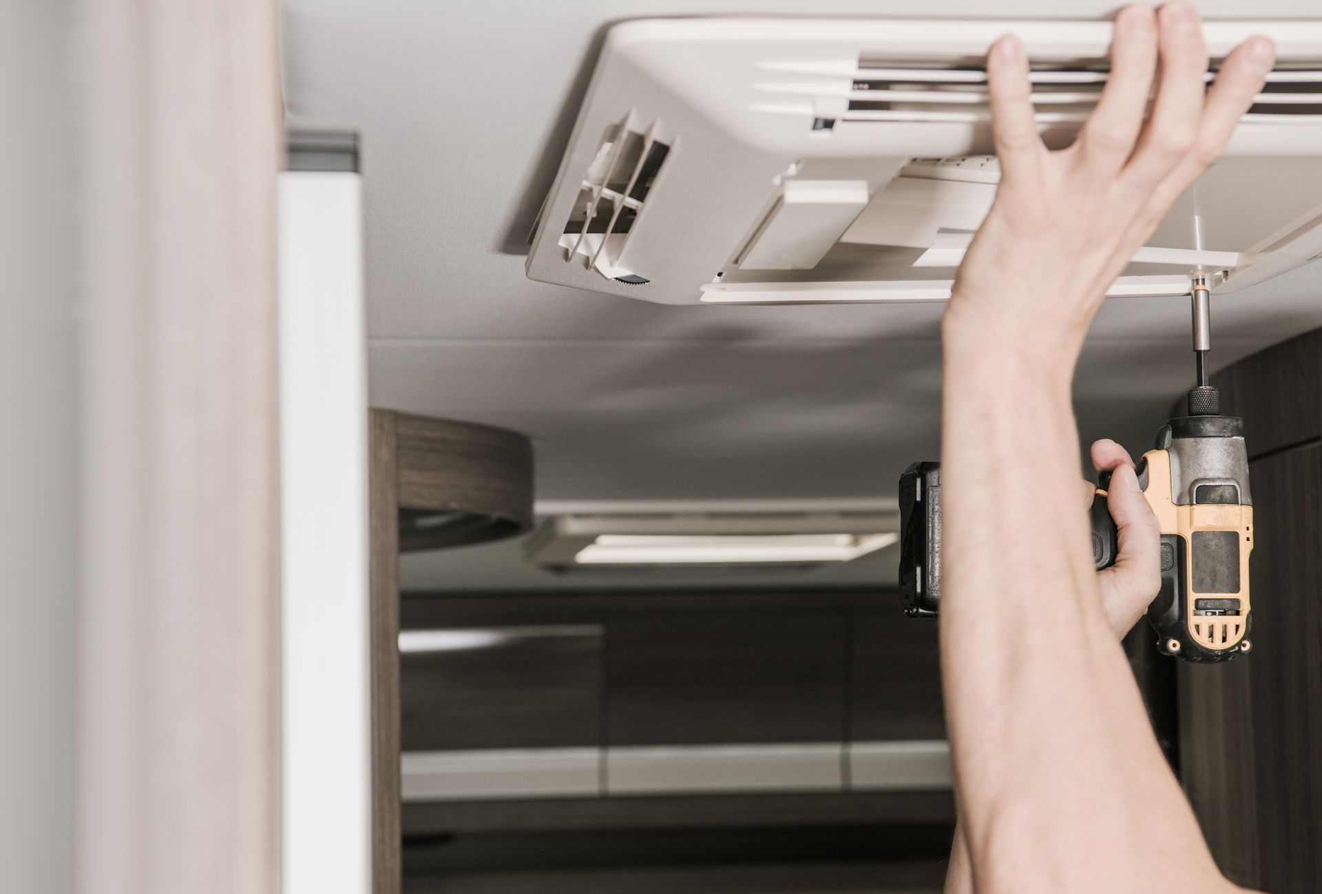 Hands repairing an overhead cabin panel with a screwdriver and hanging light bulb in a vehicle interior