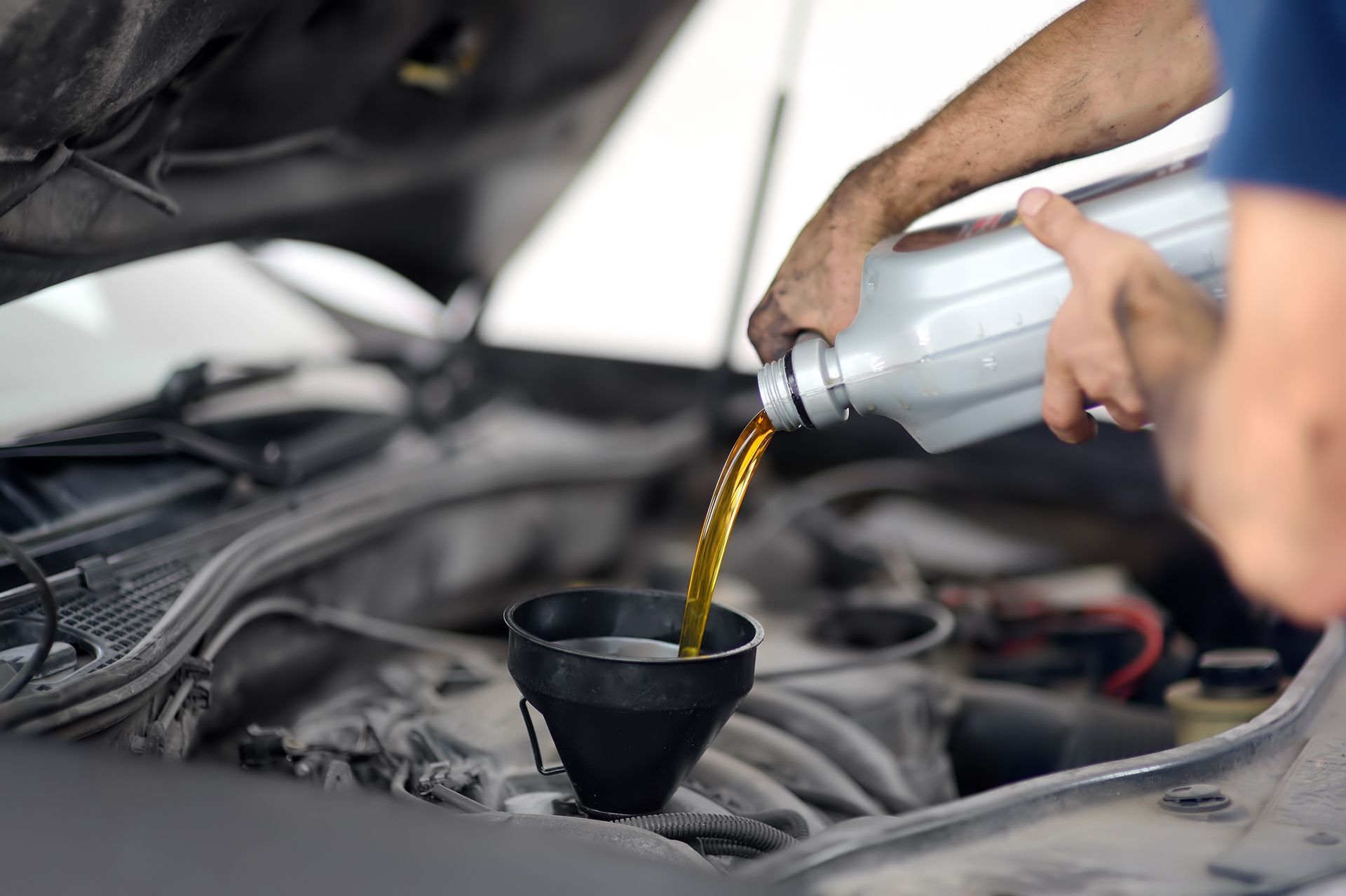 Motor oil being poured from a bottle into a funnel in a car engine bay