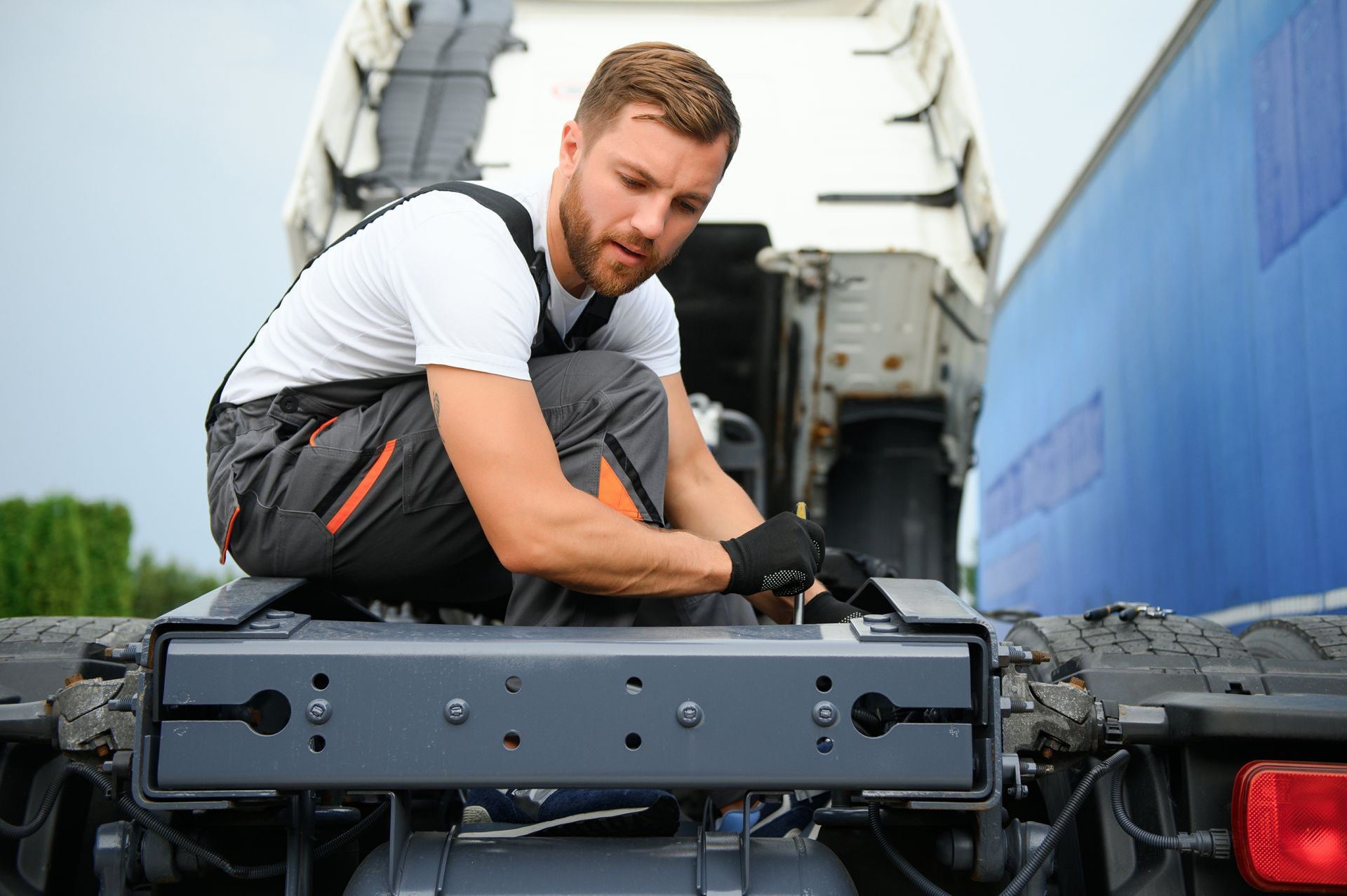Mechanic kneeling on a truck bed, tightening a black equipment rack in a transport vehicle.