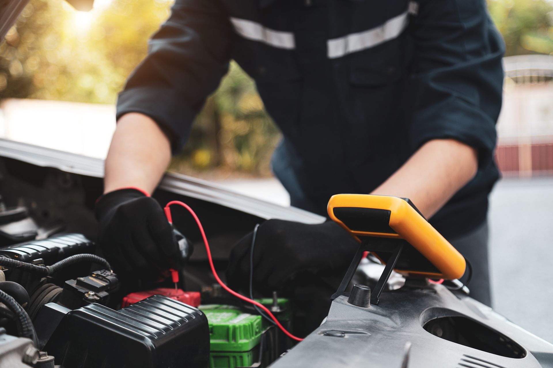 Person checking a car engine with red cables and an orange tool under the hood