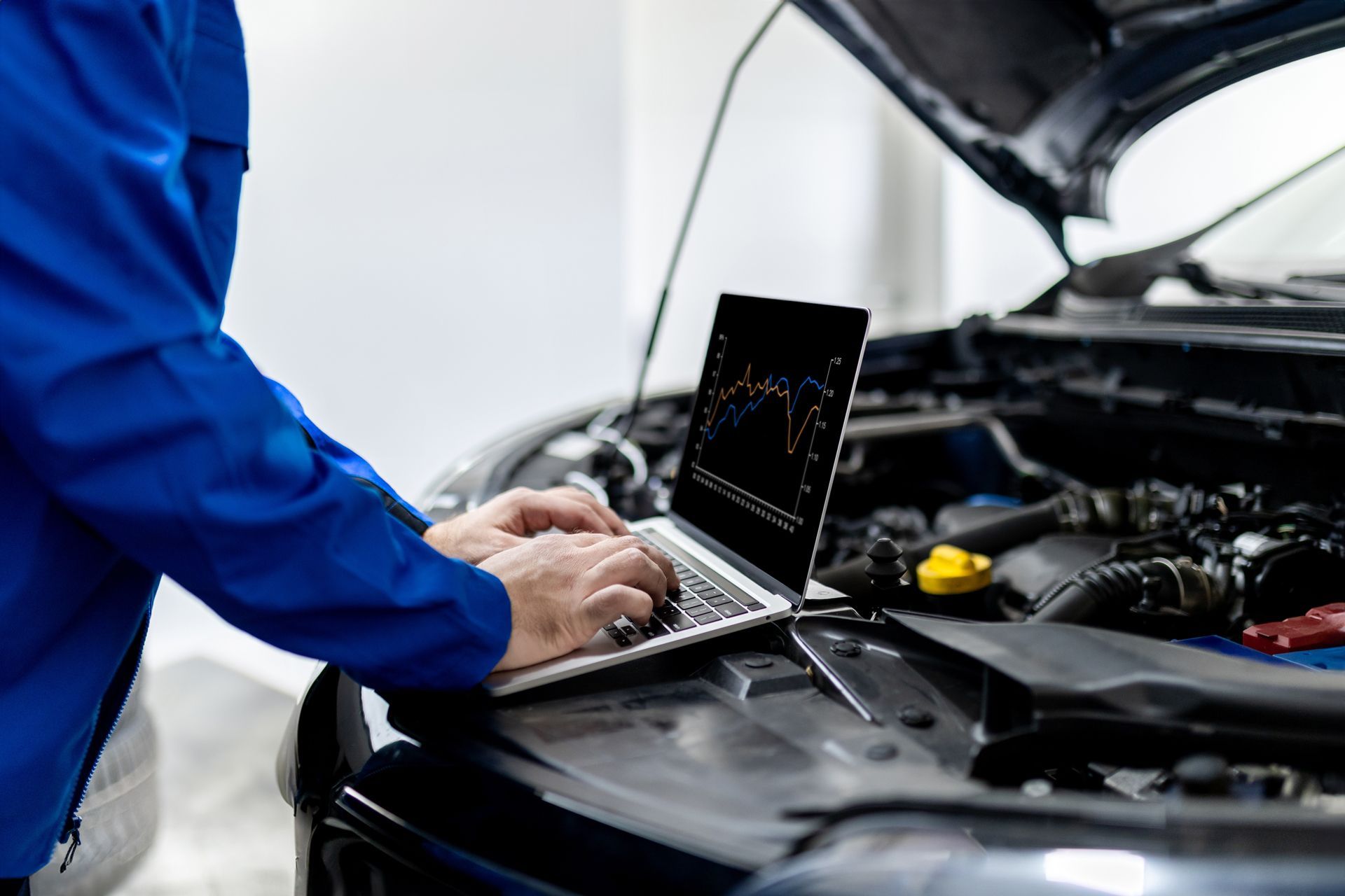 Mechanic using a laptop to diagnose a car with the hood open in a garage