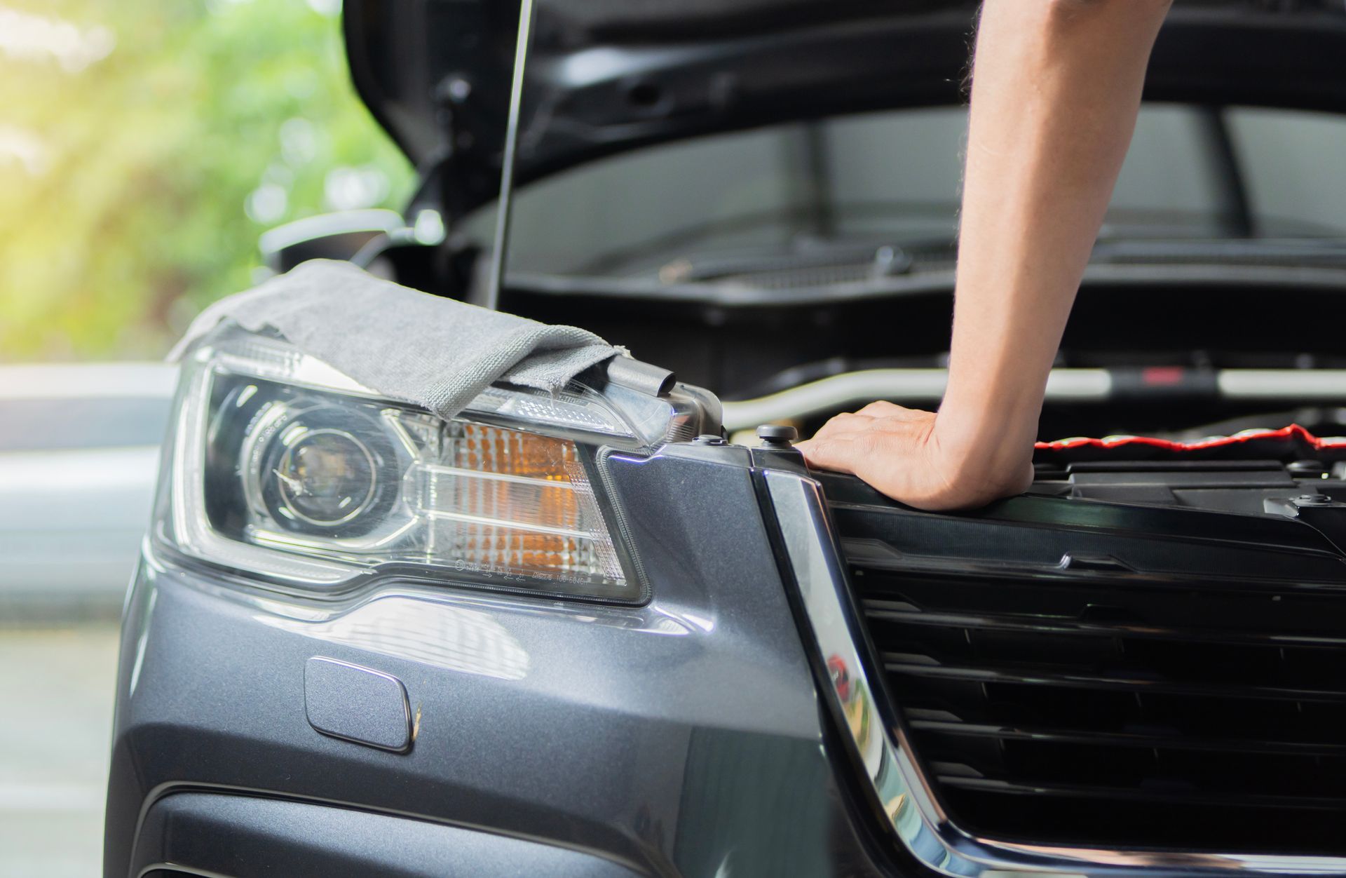 Person inspecting a gray car with the hood open, hand resting near the front grille.