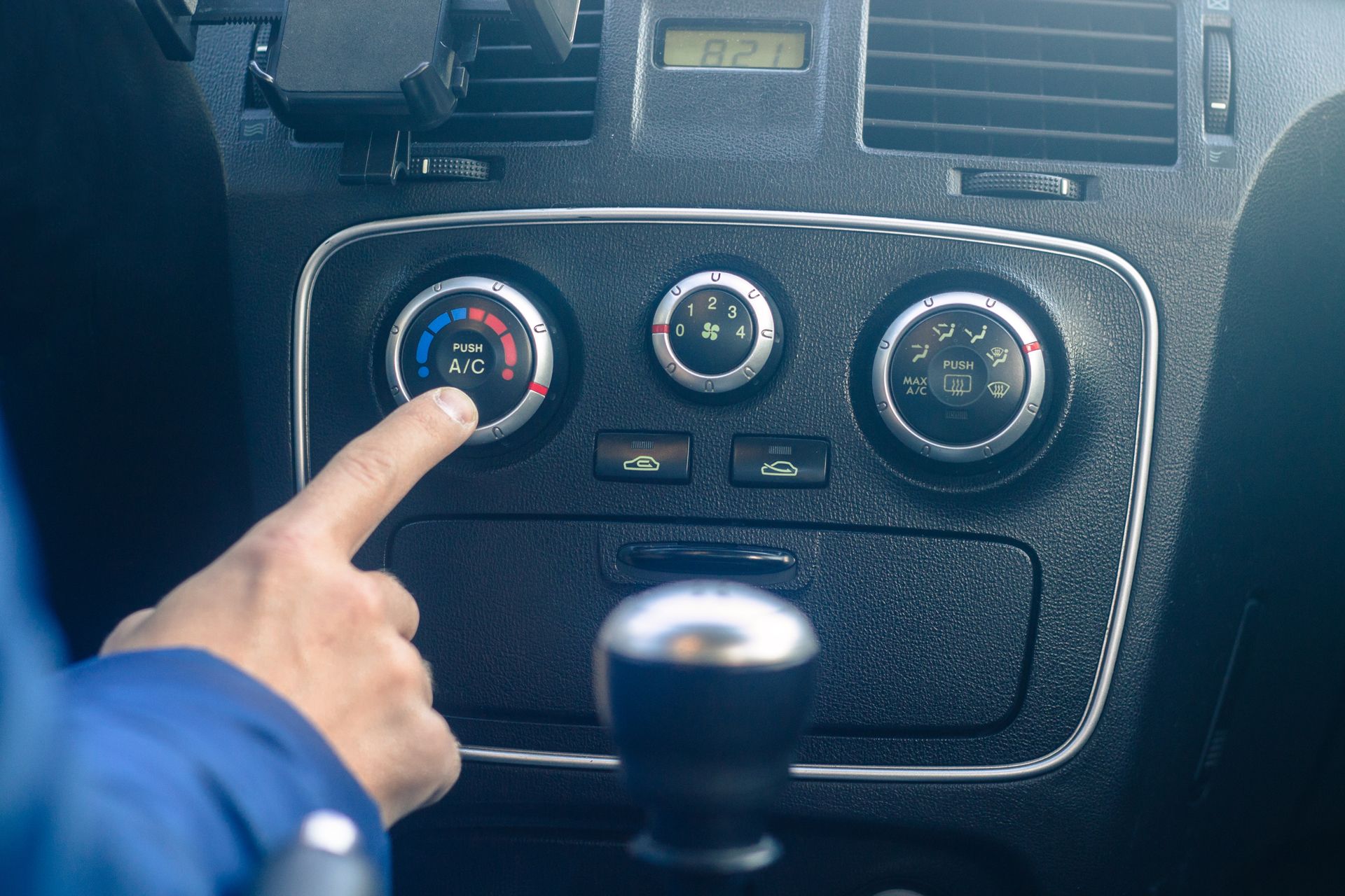 Hand pointing at a car dashboard climate control knob with blue and red temperature markings