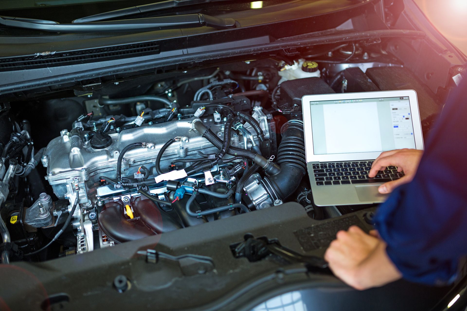 Mechanic using a laptop to diagnose a car engine in the open hood bay