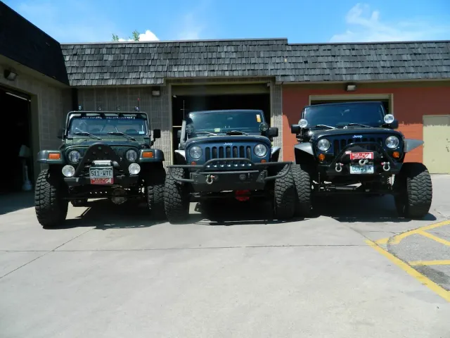 Three lifted off-road jeeps parked side by side in front of a garage
