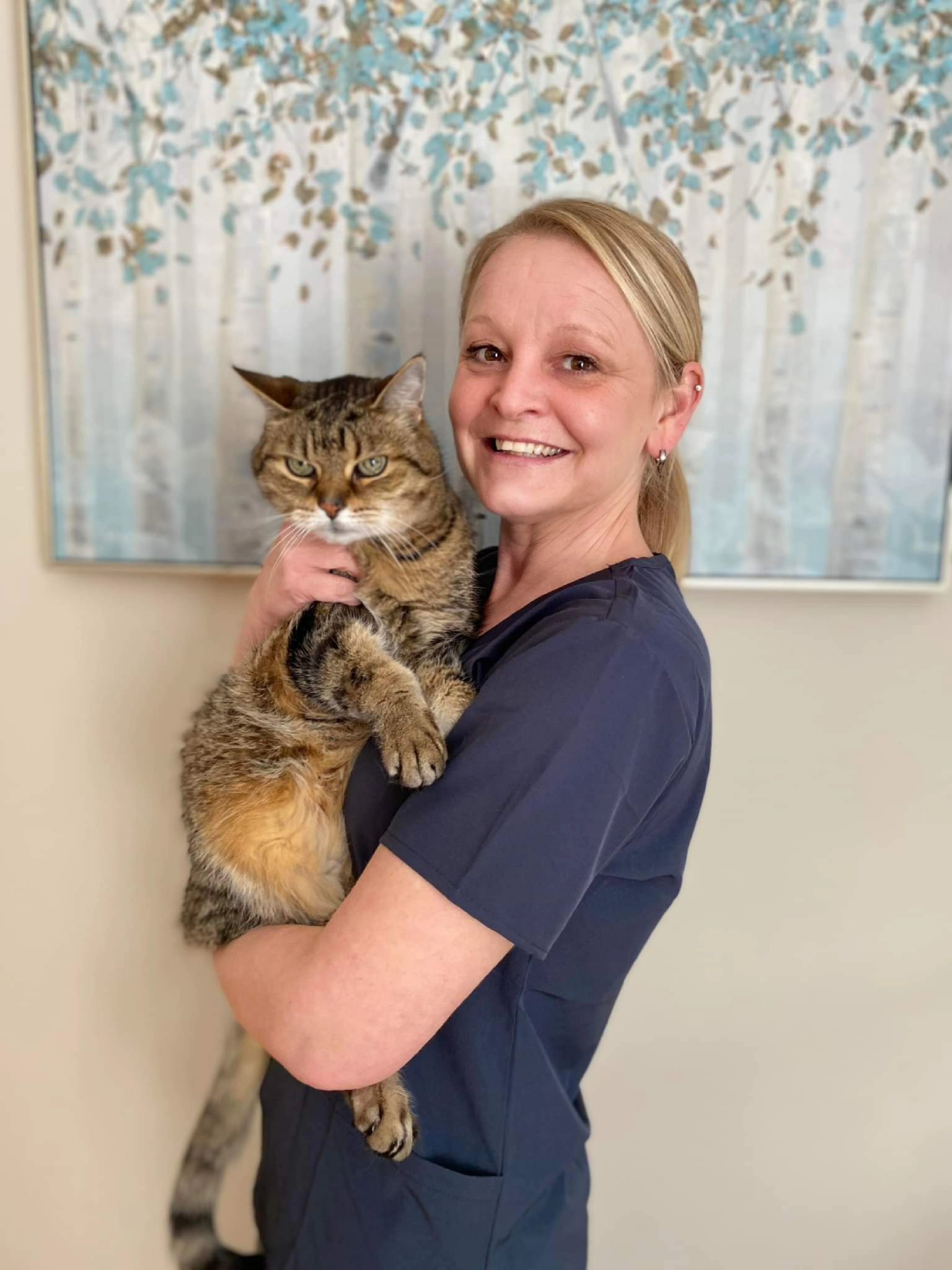 Woman in navy scrubs holding a tabby cat