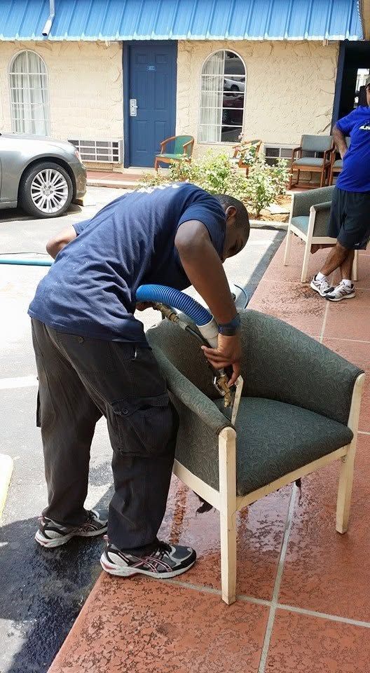 Person sanding a green chair on a patio while another person stands nearby.