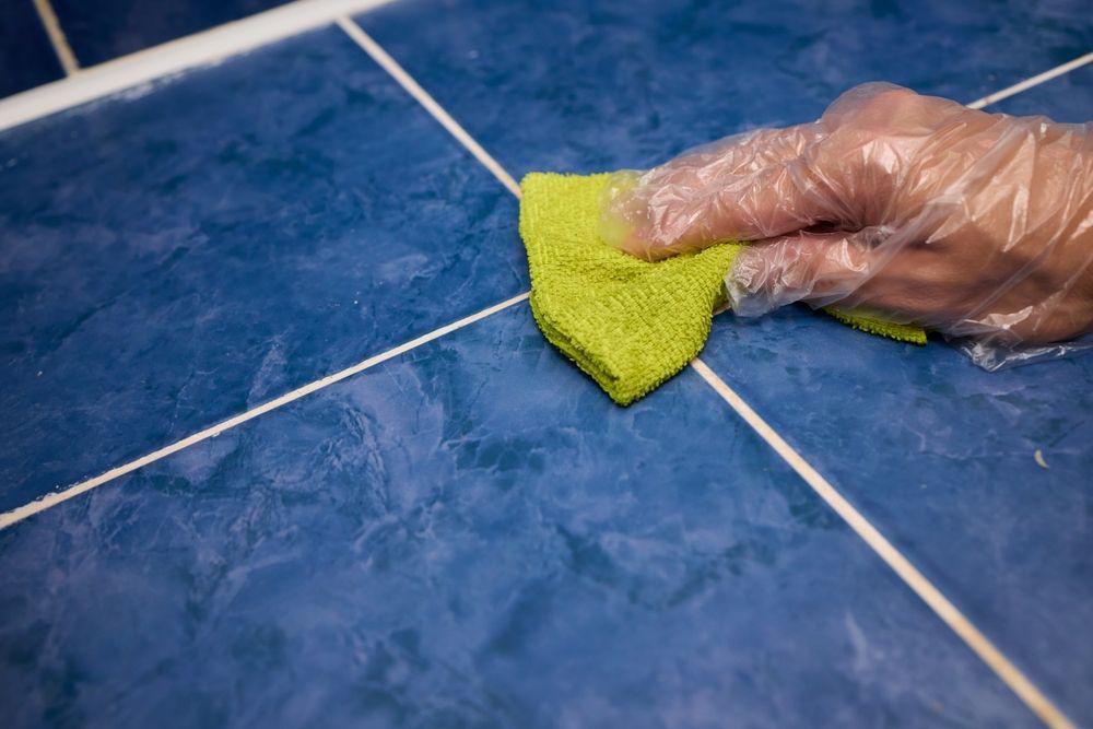 Gloved hand wiping blue tiled floor with a green cloth