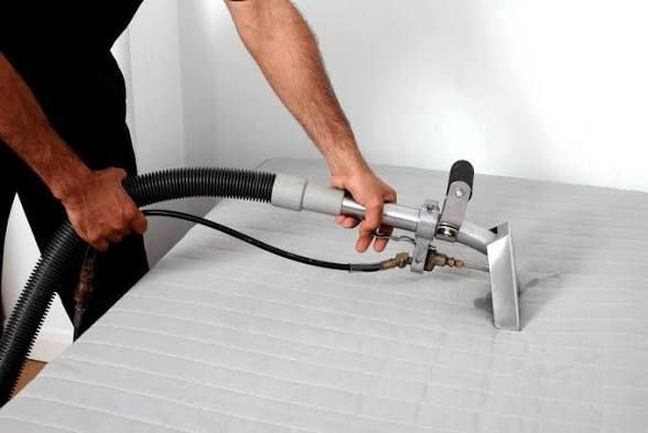A person vacuuming a white bed mattress with a handheld upholstery tool in a bedroom