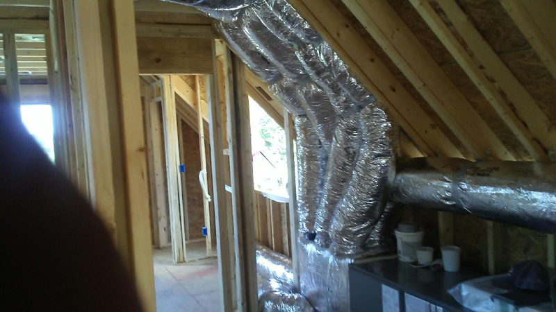 Interior view of a building under construction, showing ductwork installation and wooden framing.