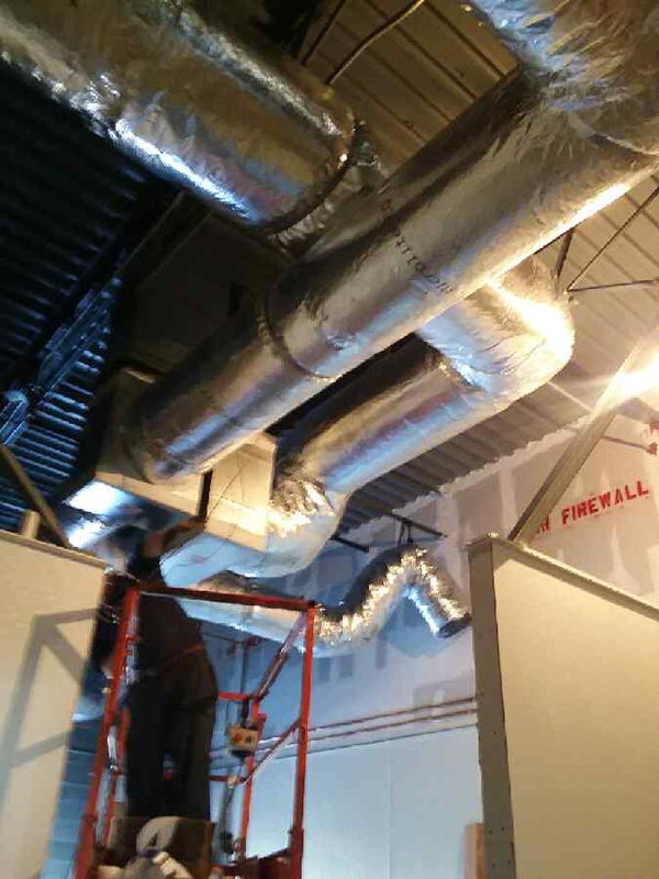 HVAC ductwork installation in a building under construction; worker on a lift.