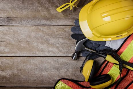 Construction hard hat, gloves, and safety harness on weathered wooden boards.
